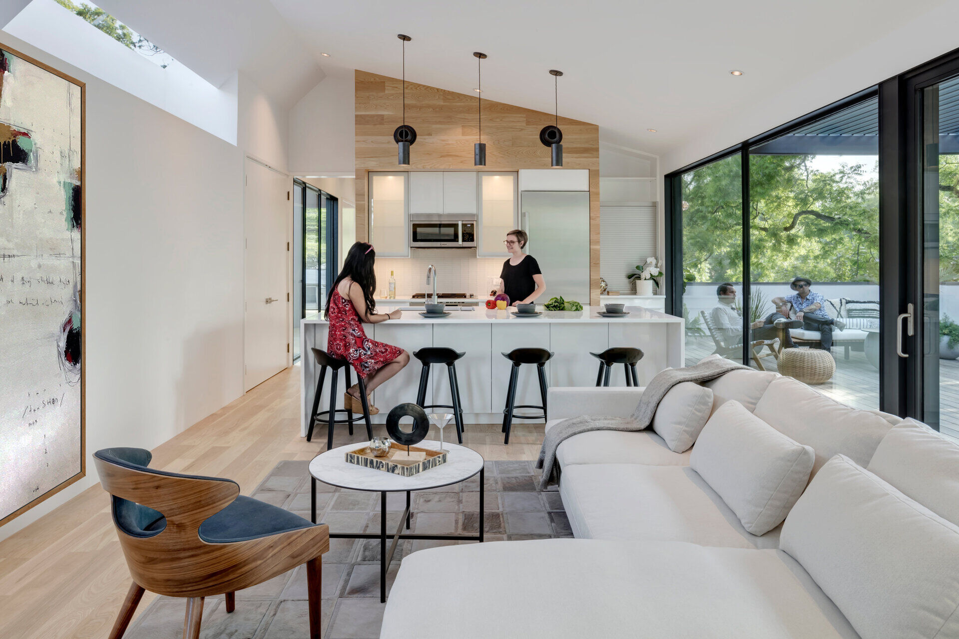The living room and kitchen share one airy space, softened by wood flooring and a warm accent wall that balance the clean white surfaces.