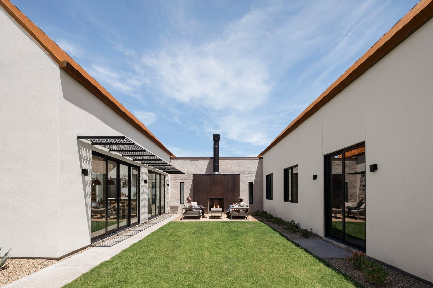 A rusted steel fireplace anchors the central courtyard, creating an outdoor lounge that links the living and sleeping wings of the home.