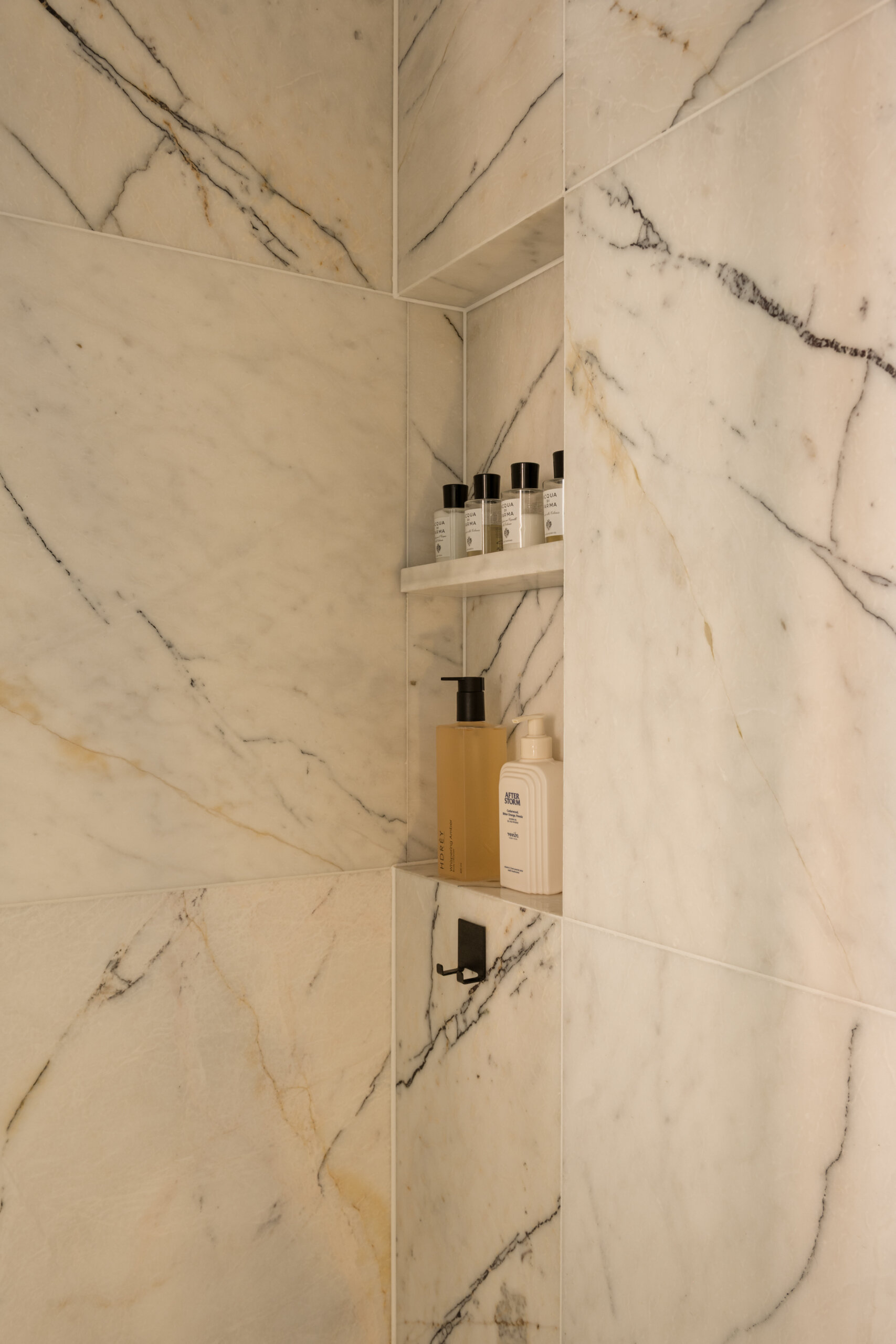 A mirrored cube hides an entire bathroom and wardrobe in plain sight. Its reflections expand the small apartment, while inside, white Calacatta Lilac marble and soft backlighting make the space feel impossibly bright and tall.