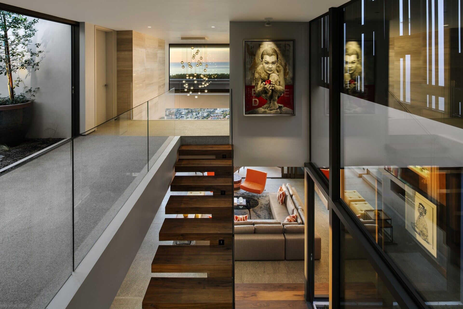 Wood and black metal stairs, paired with invisible glass railings, lead to the upper floor, where a landing overlooks both the living room and courtyard.