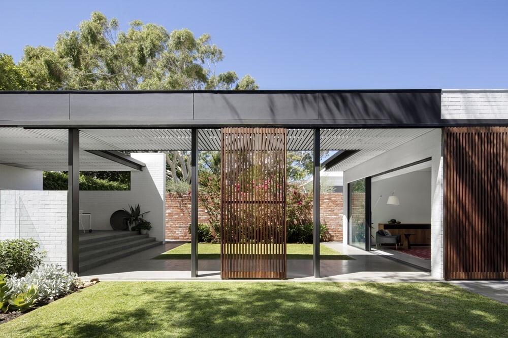 A refined modern house extension  with white brick volumes and dark steel and wood accents surrounded by lush gardens.