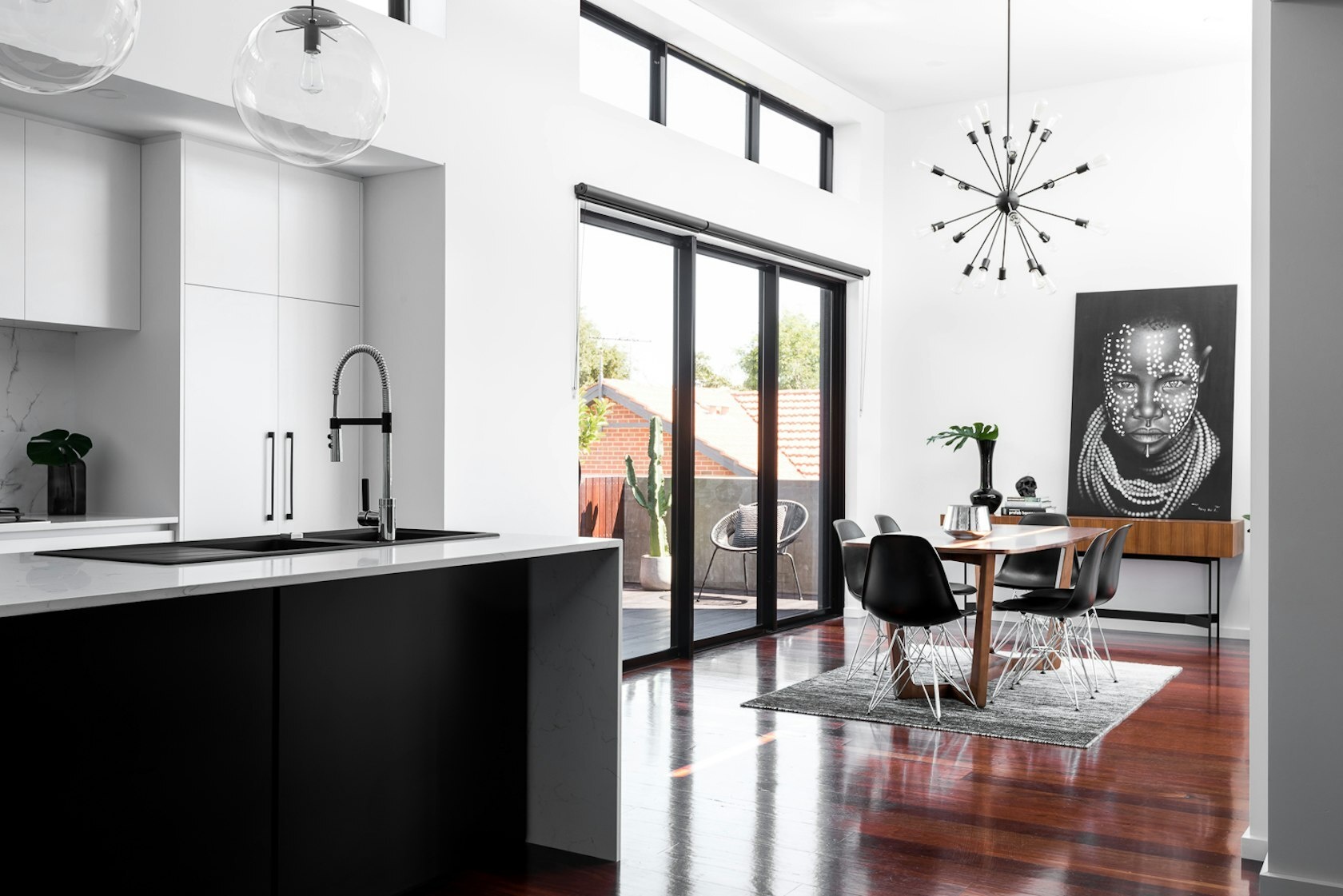 This bright modern kitchen balances white cabinetry with a bold black island, opening onto a dining room framed by sliding doors and high ceilings.