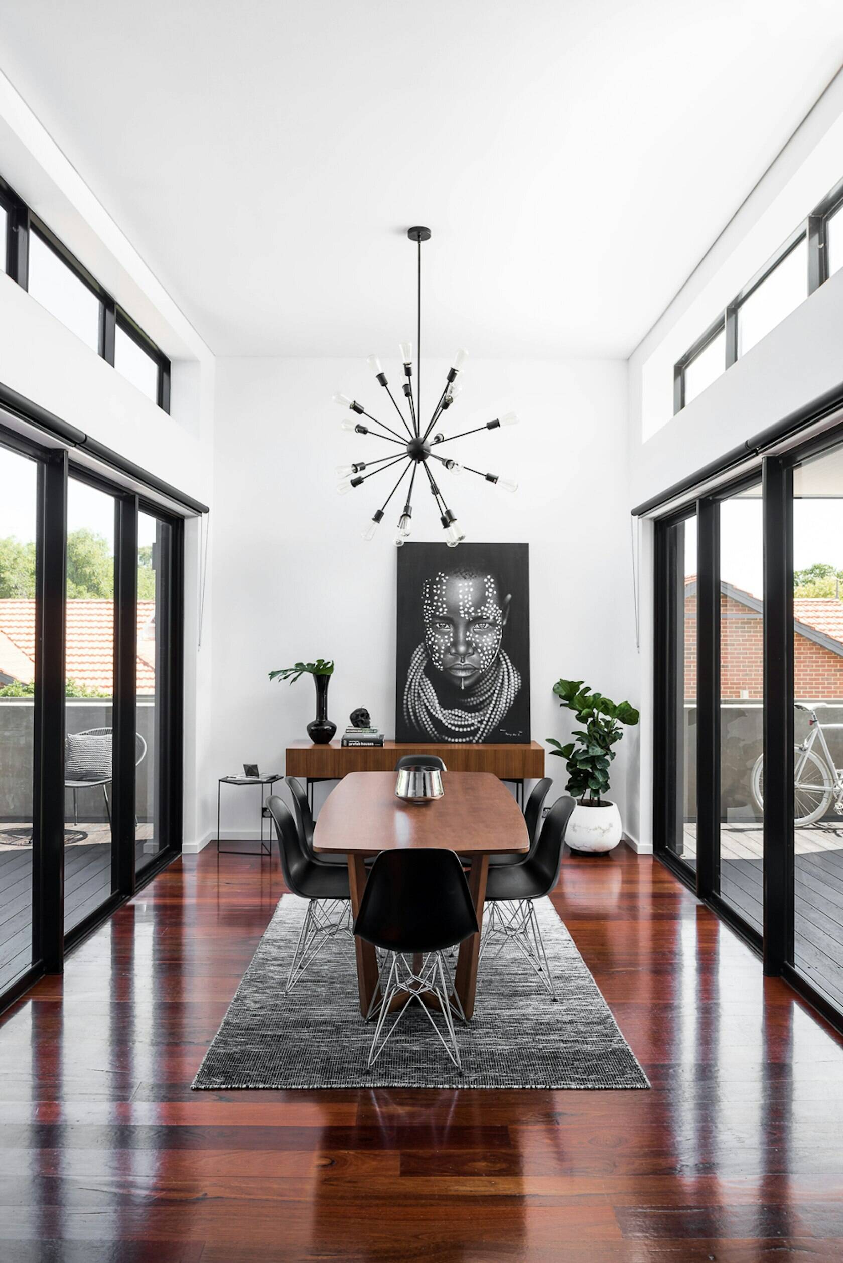 This bright modern kitchen balances white cabinetry with a bold black island, opening onto a dining room framed by sliding doors and high ceilings.
