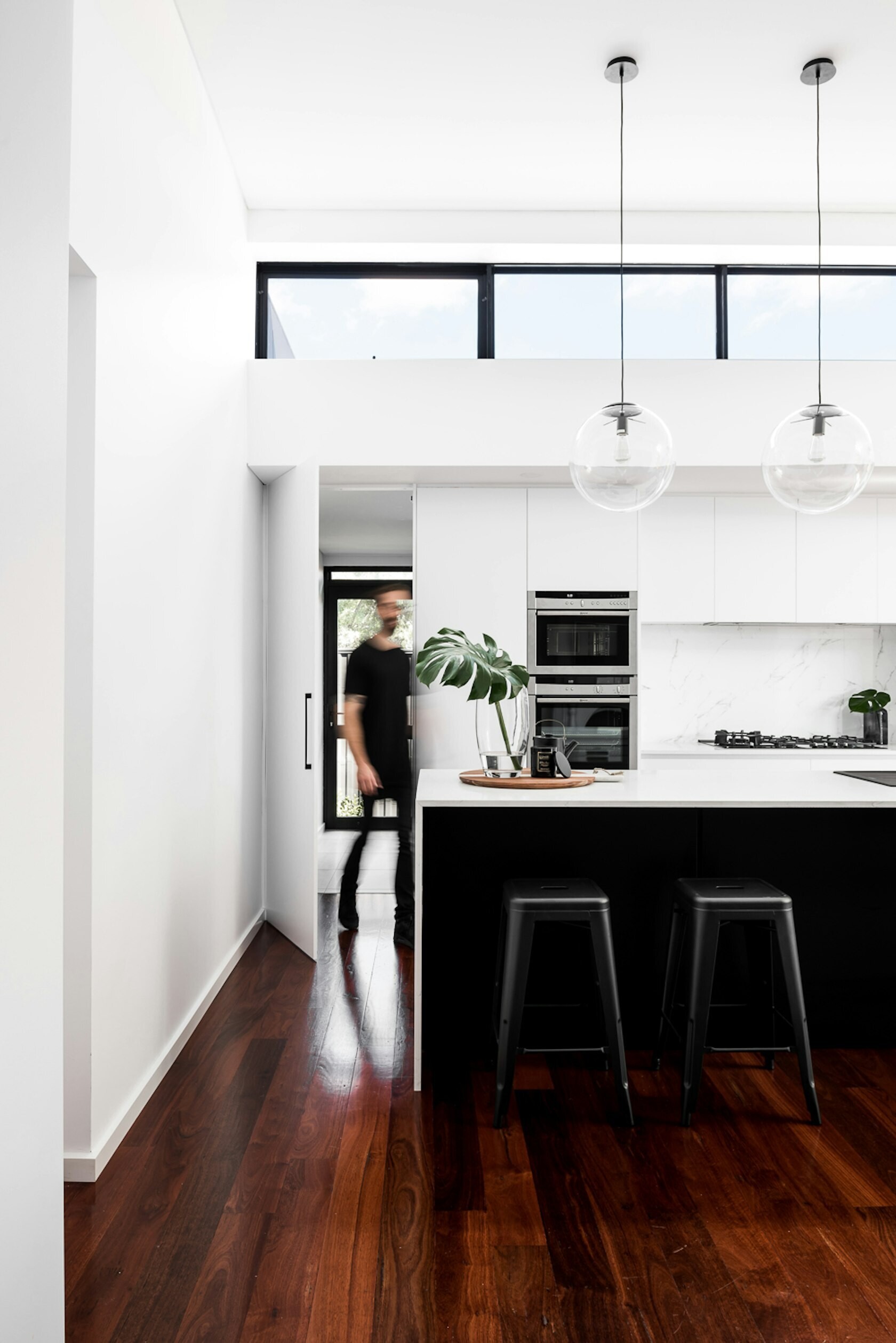 This bright modern kitchen balances white cabinetry with a bold black island, opening onto a dining room framed by sliding doors and high ceilings.