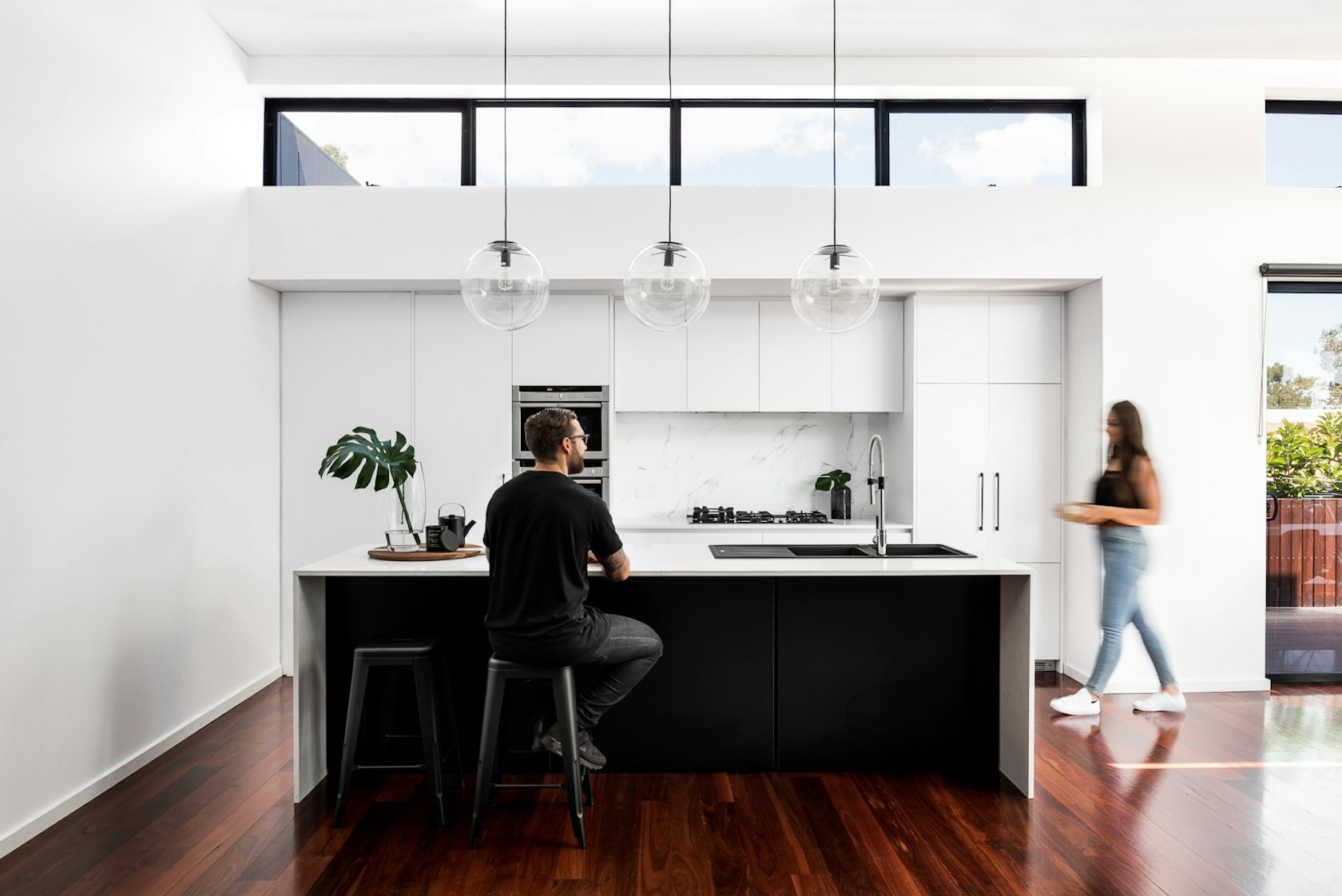 This bright modern kitchen balances white cabinetry with a bold black island, opening onto a dining room framed by sliding doors and high ceilings.