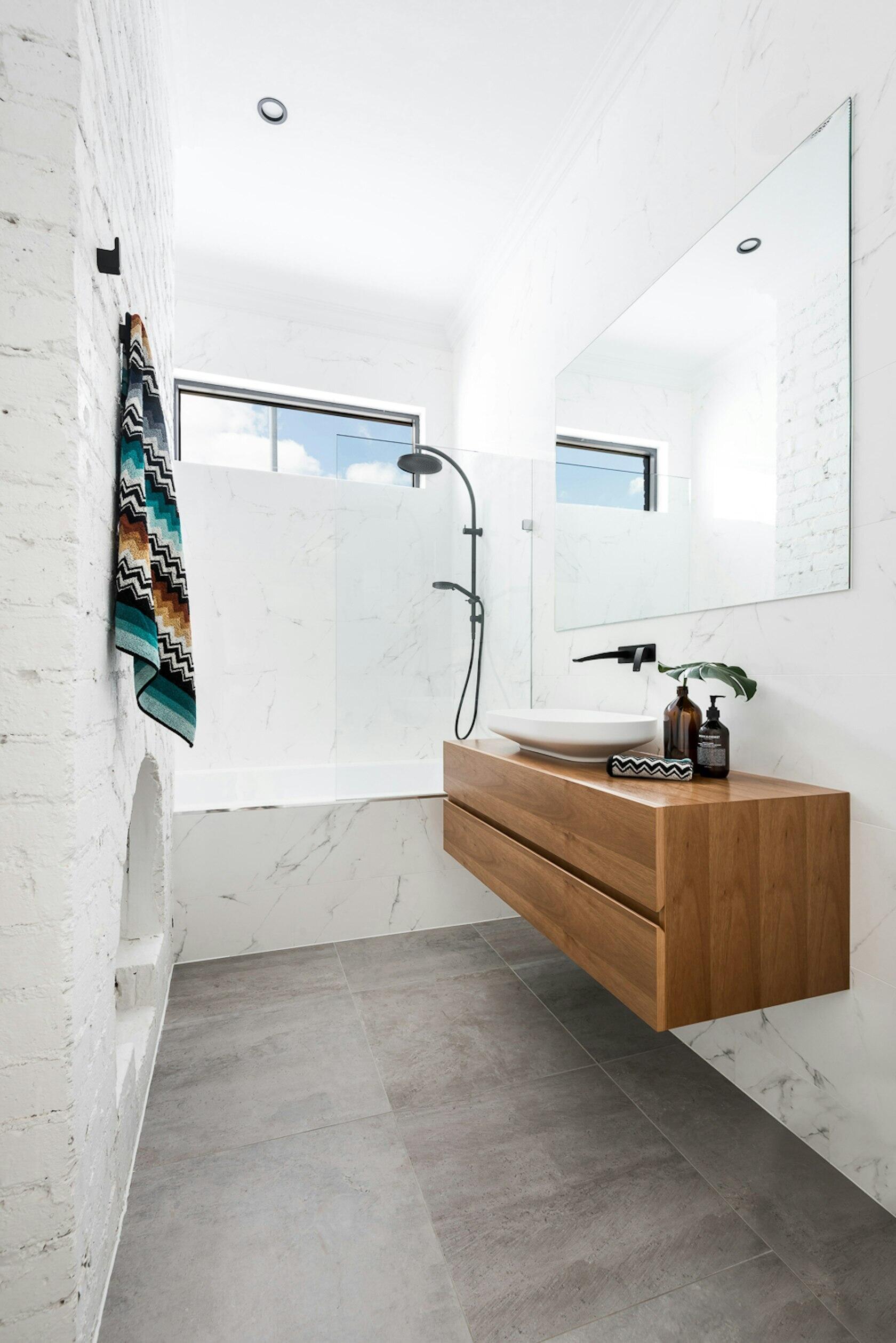 This contemporary bathroom highlights an original fireplace as a feature, a beautiful reminder of the home’s century-old story, now paired with a modern floating wood vanity and built-in bathtub.