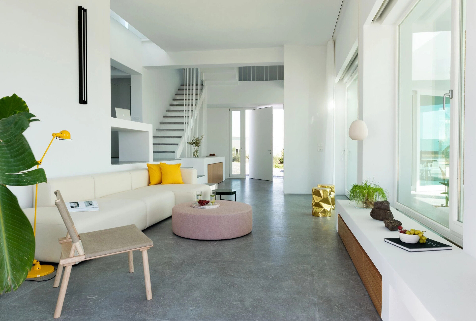 Inside, white plaster walls and grey cement floors create a calm canvas for wooden details and pops of color. The living room flows seamlessly to an outdoor lounge built around a palm tree.