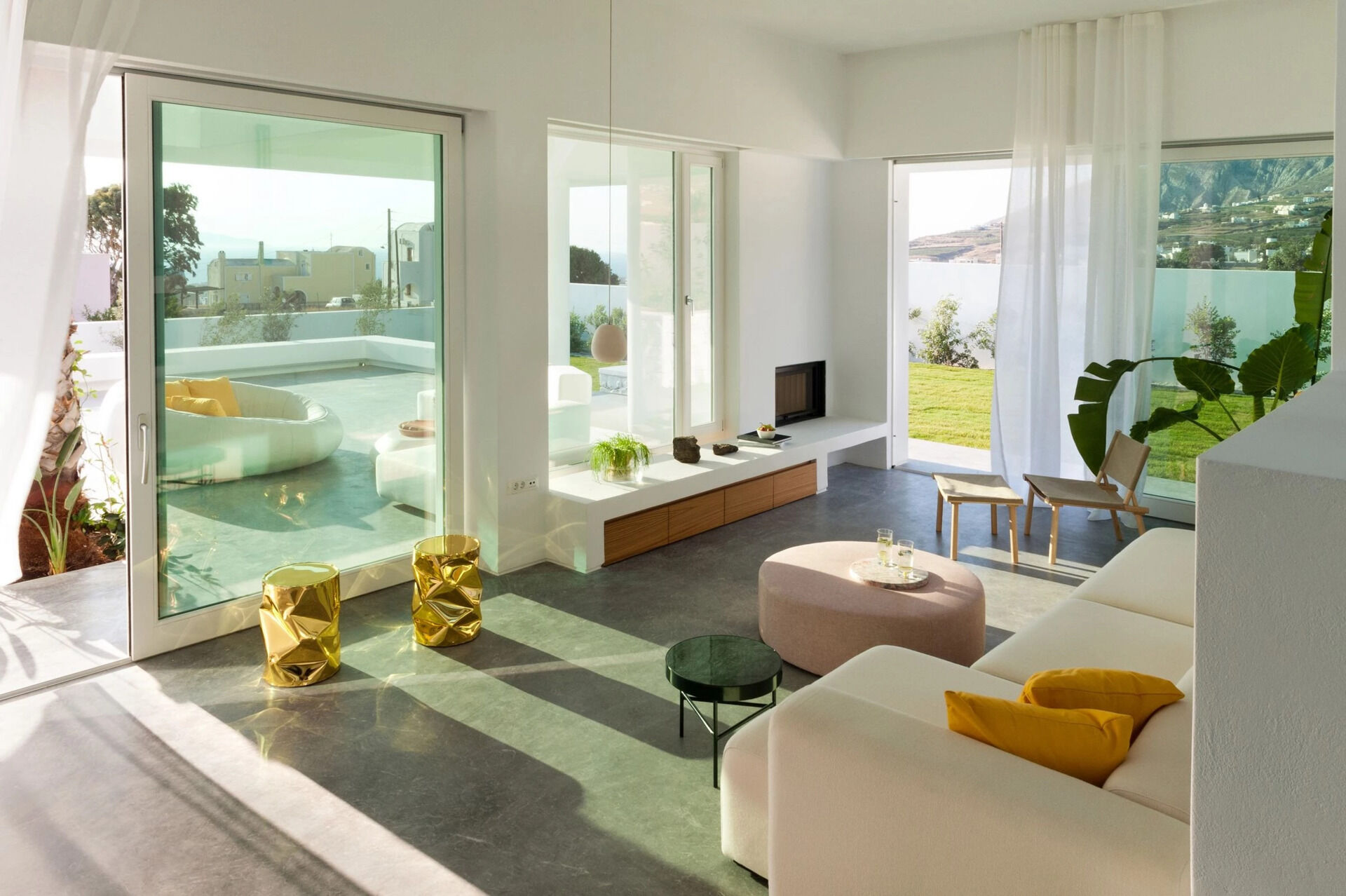 Inside, white plaster walls and grey cement floors create a calm canvas for wooden details and pops of color. The living room flows seamlessly to an outdoor lounge built around a palm tree.