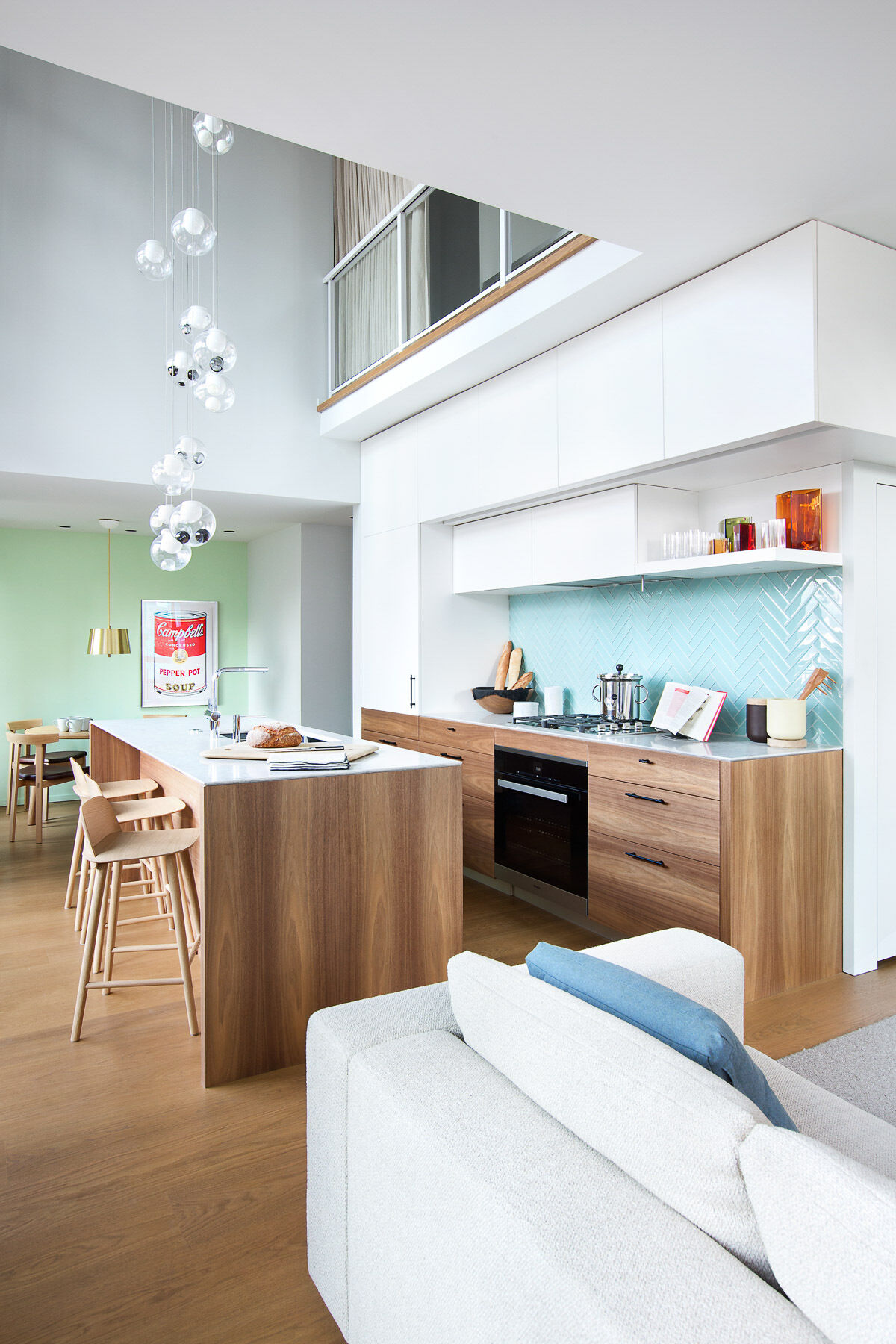 This kitchen is sleek and understated, designed to disappear when not in use. White upper cabinets flow seamlessly into matching white walls and thin countertops, blurring the line between storage and surface. The effect is calming, visually expanding the room without adding clutter.
Then comes the surprise: a backsplash of bright blue tiles. Against the neutral surroundings, that single block of color becomes the focal point, confident but controlled.