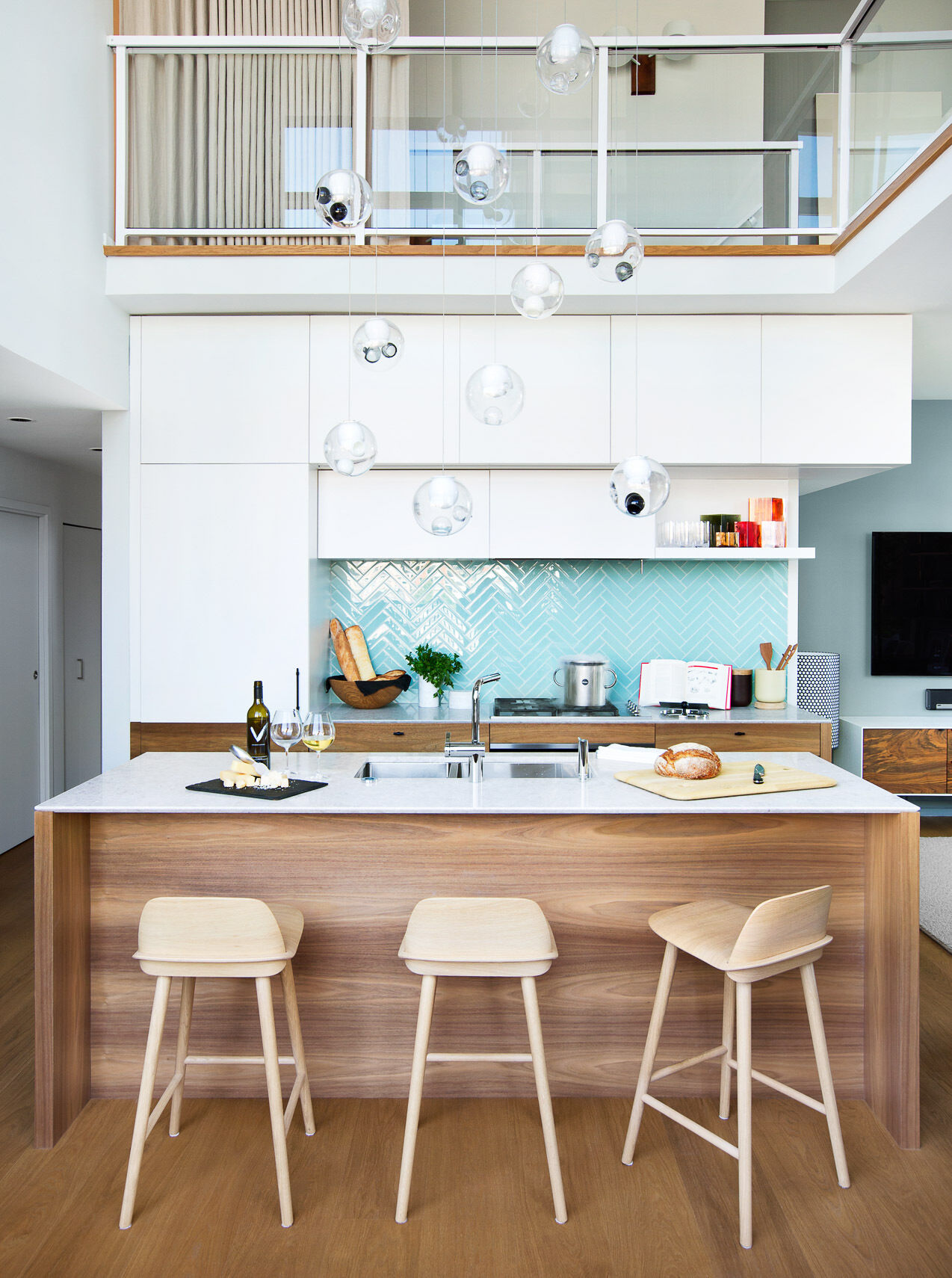 This kitchen is sleek and understated, designed to disappear when not in use. White upper cabinets flow seamlessly into matching white walls and thin countertops, blurring the line between storage and surface. The effect is calming, visually expanding the room without adding clutter.
Then comes the surprise: a backsplash of bright blue tiles. Against the neutral surroundings, that single block of color becomes the focal point, confident but controlled.