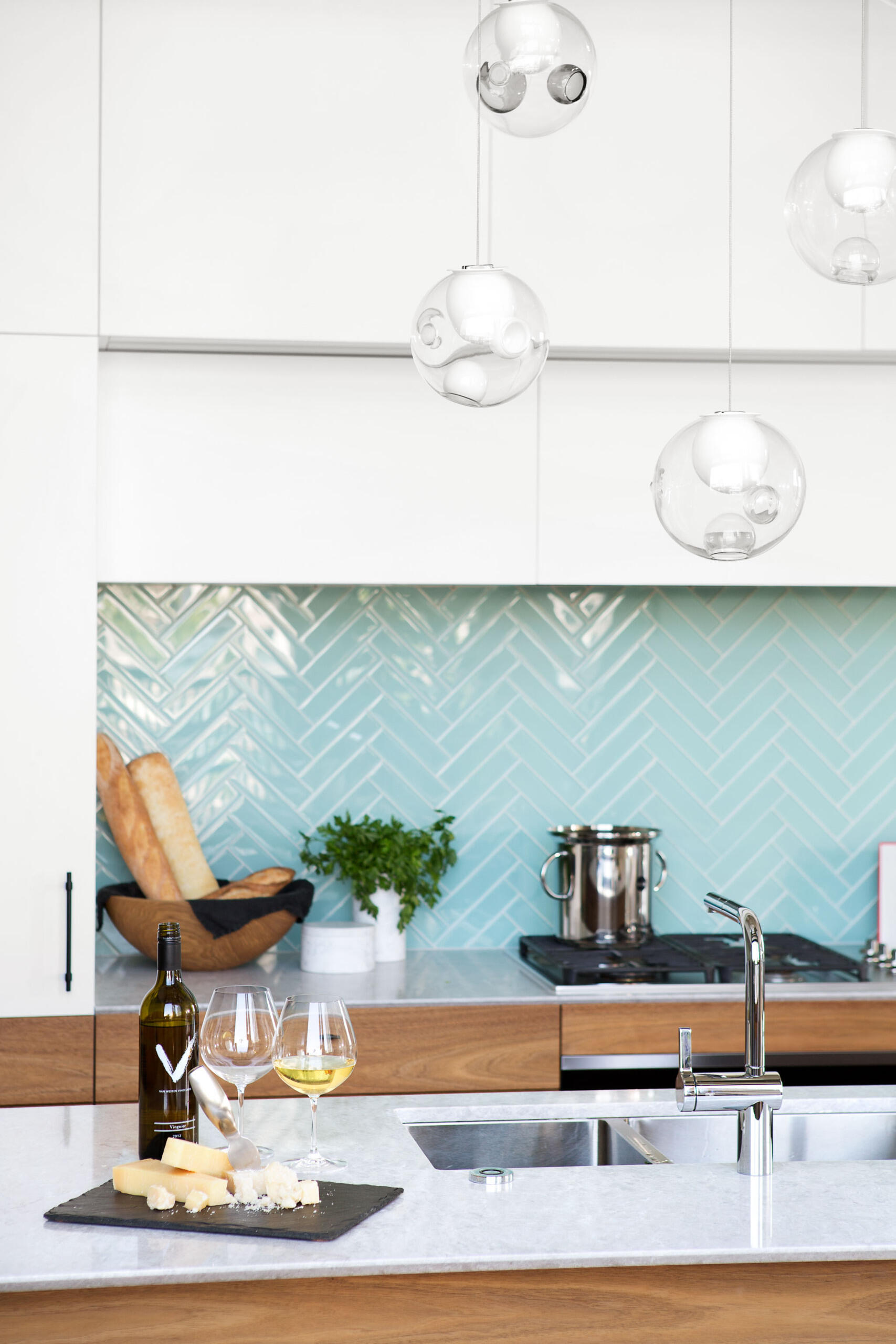 This kitchen is sleek and understated, designed to disappear when not in use. White upper cabinets flow seamlessly into matching white walls and thin countertops, blurring the line between storage and surface. The effect is calming, visually expanding the room without adding clutter.
Then comes the surprise: a backsplash of bright blue tiles. Against the neutral surroundings, that single block of color becomes the focal point, confident but controlled.