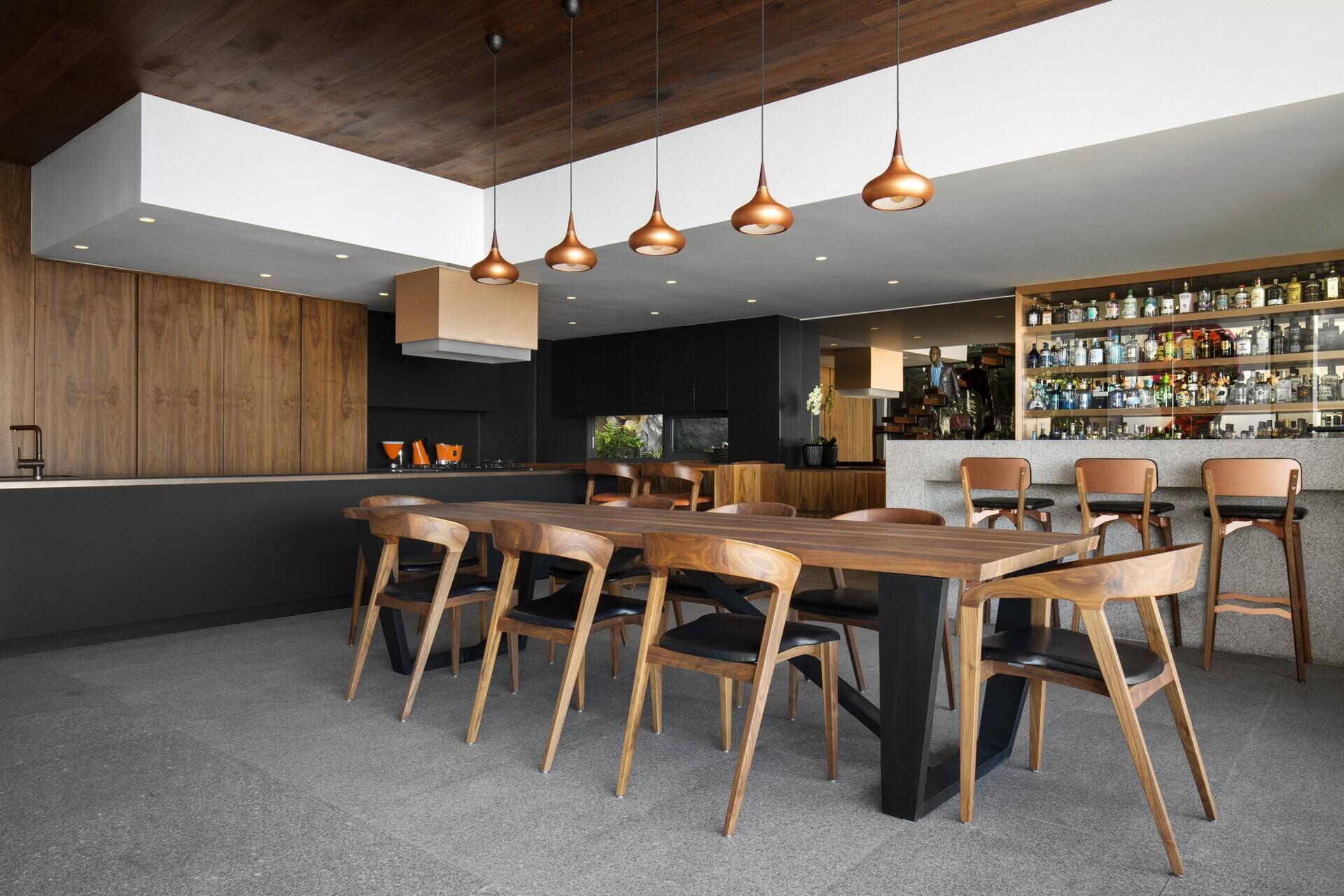 Long wood dining table with a black base perfect for formal dinners or casual gatherings, complemented by a bar area.