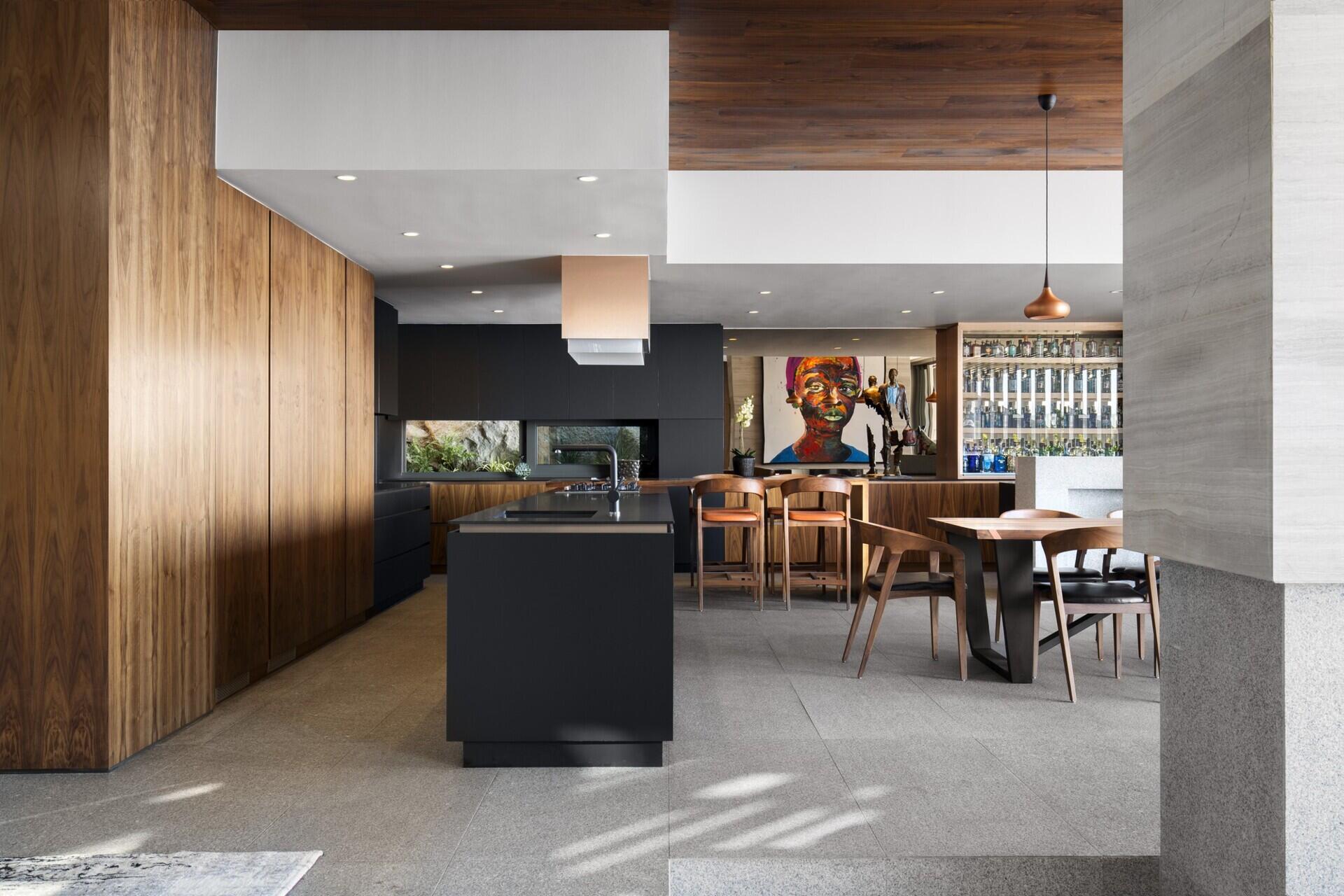 Sleek black-and-wood kitchen with long island and hidden appliances, blending functionality with style.