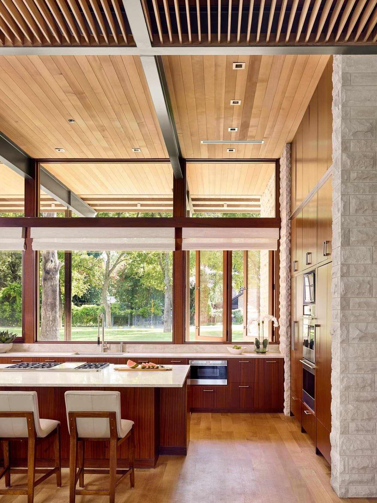 The kitchen’s warm wood cabinetry and light countertops complement the limestone palette, flowing seamlessly into the dining space.