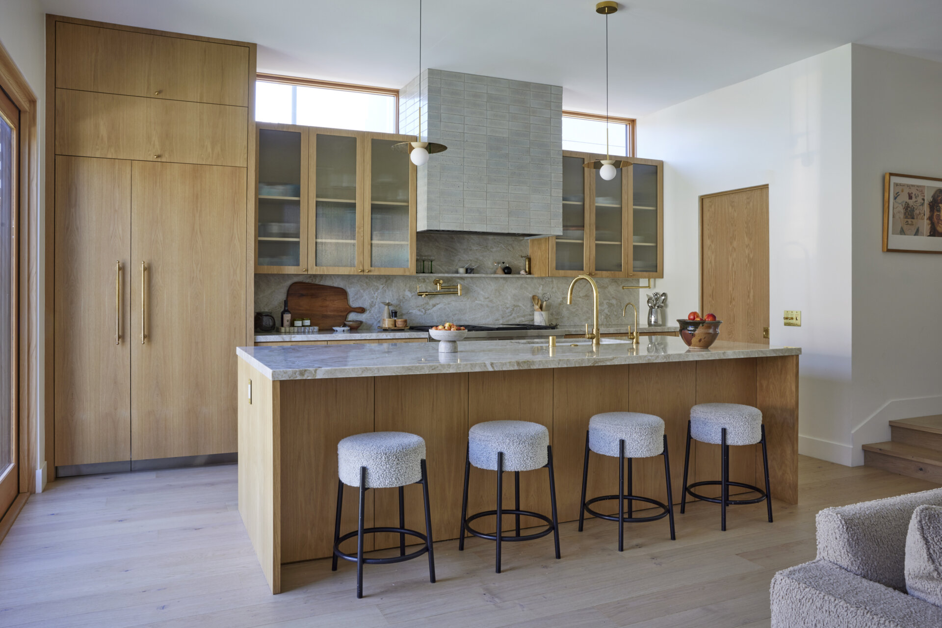 The kitchen shines with a marble-topped island, brass fixtures, and wood cabinetry, while the wallpapered pantry adds an unexpected design surprise.