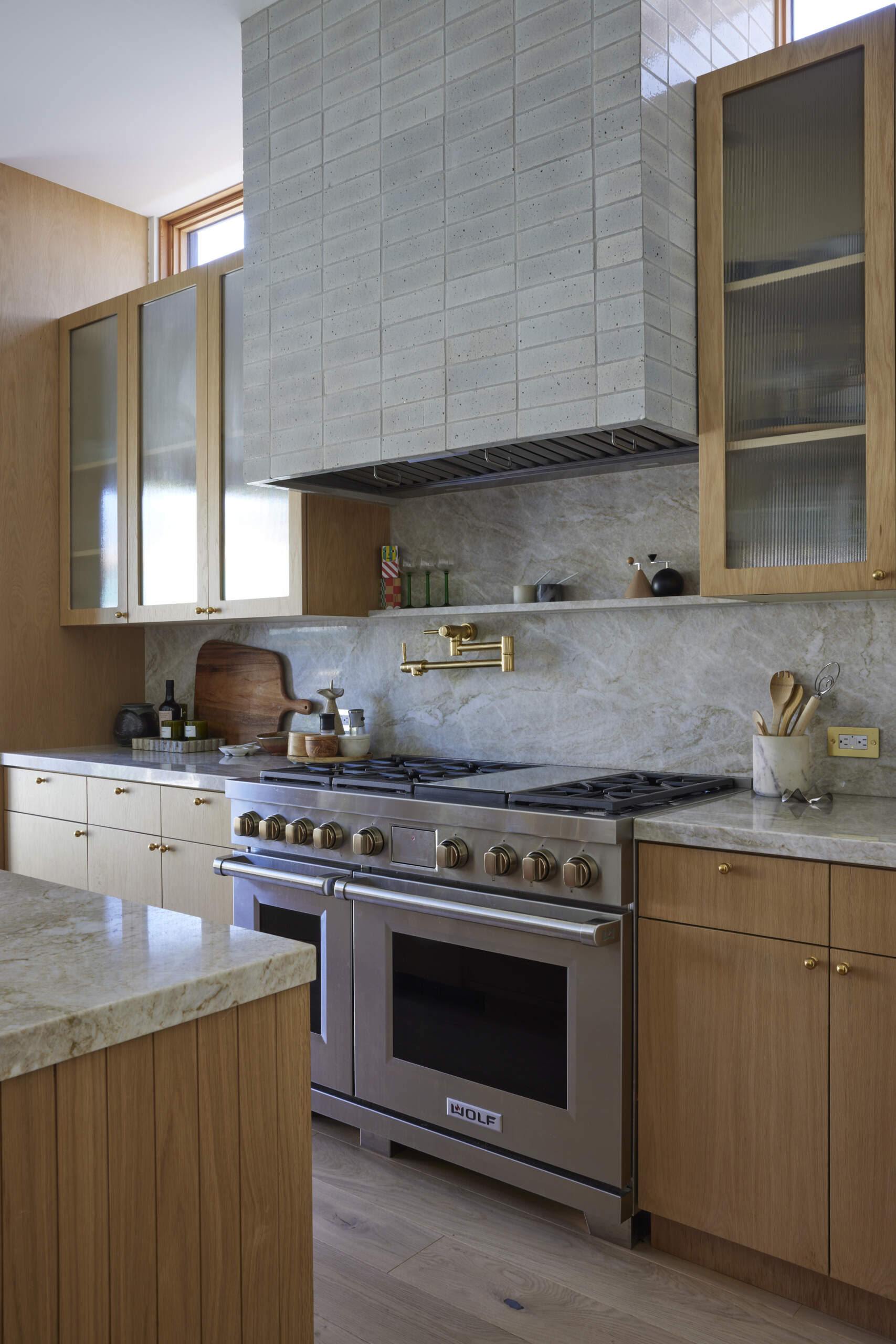 The kitchen shines with a marble-topped island, brass fixtures, and wood cabinetry, while the wallpapered pantry adds an unexpected design surprise.