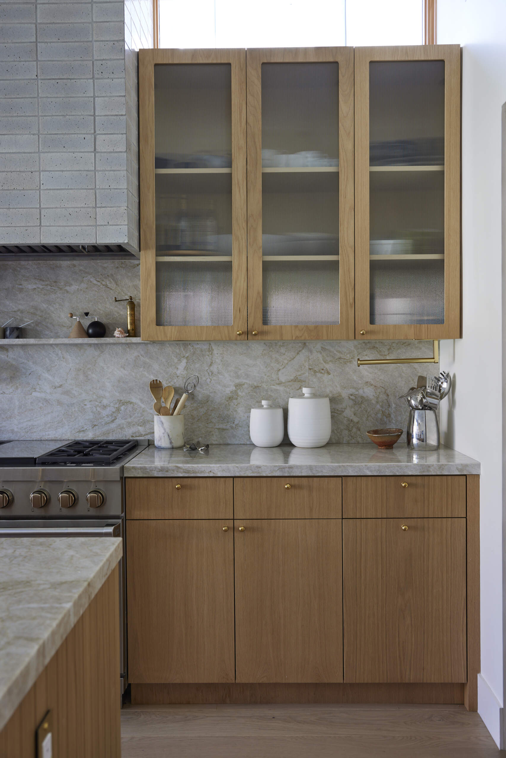 The kitchen shines with a marble-topped island, brass fixtures, and wood cabinetry, while the wallpapered pantry adds an unexpected design surprise.