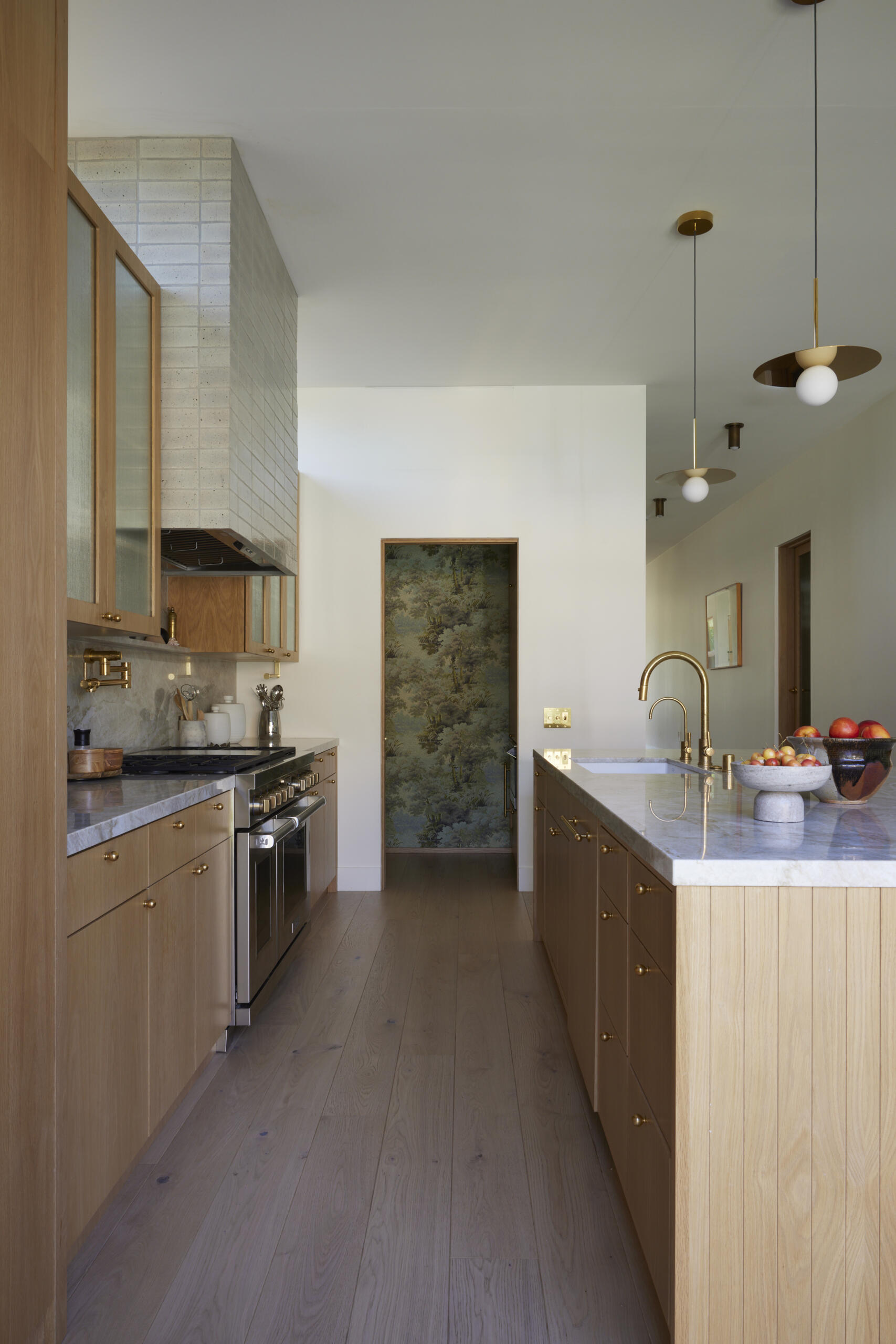 The kitchen shines with a marble-topped island, brass fixtures, and wood cabinetry, while the wallpapered pantry adds an unexpected design surprise.