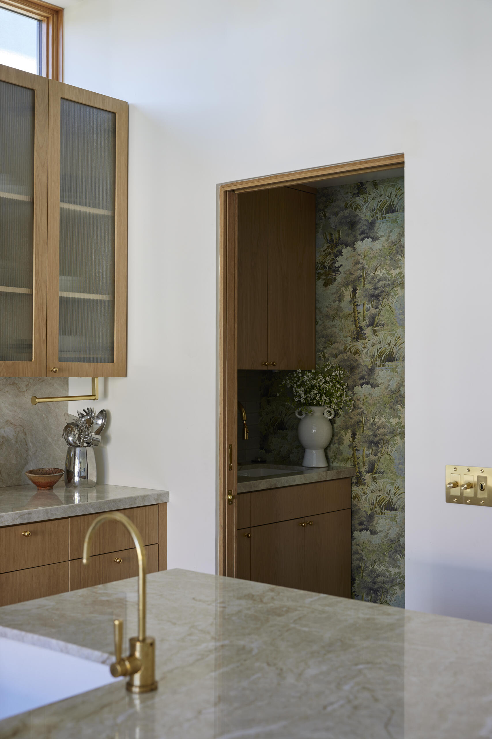The kitchen shines with a marble-topped island, brass fixtures, and wood cabinetry, while the wallpapered pantry adds an unexpected design surprise.