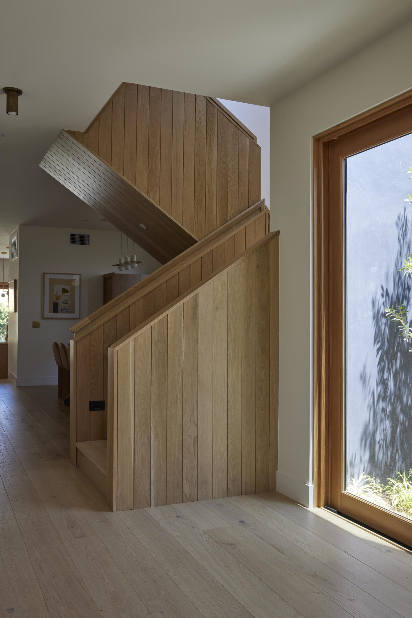 The sculptural white oak staircase doubles as art, featuring a playful round peek-a-boo cutout that adds a lighthearted touch.