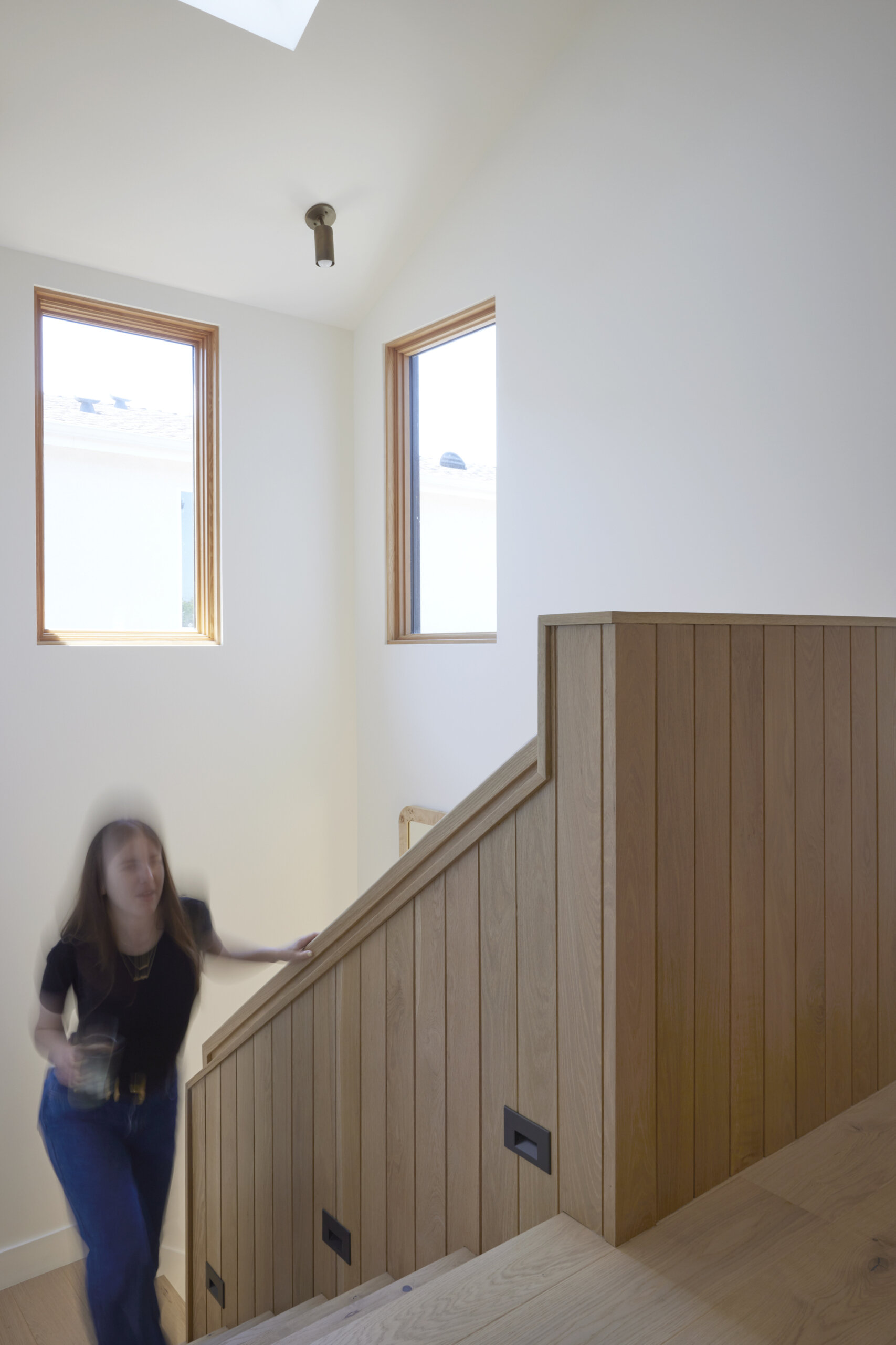 The sculptural white oak staircase doubles as art, featuring a playful round peek-a-boo cutout that adds a lighthearted touch.