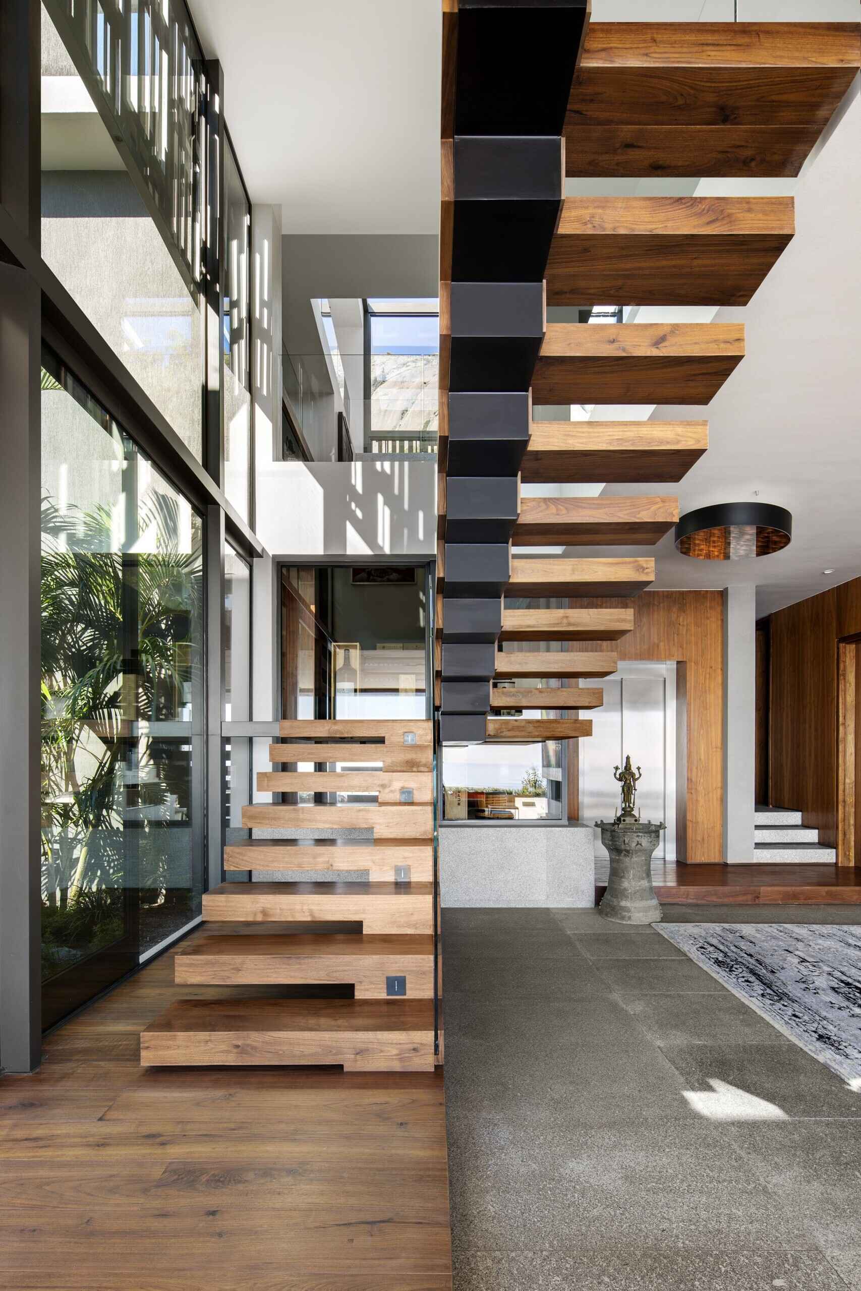 Wood and black metal stairs, paired with invisible glass railings, lead to the upper floor, where a landing overlooks both the living room and courtyard.