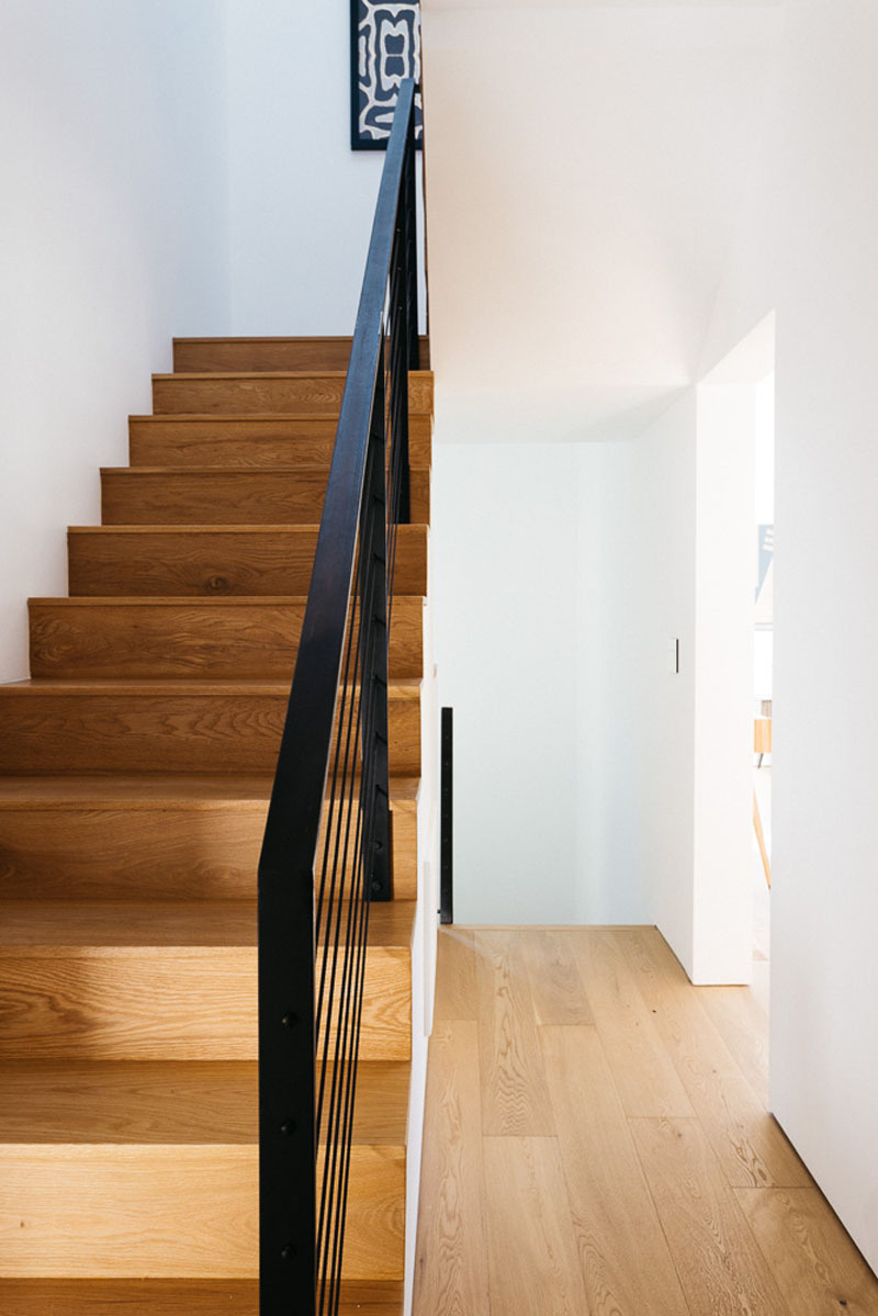 A simple wood staircase with a black handrail ties the home’s levels together. The stairwell doubles as a light well, its openness and verticality creating a calm rhythm as you move between floors.