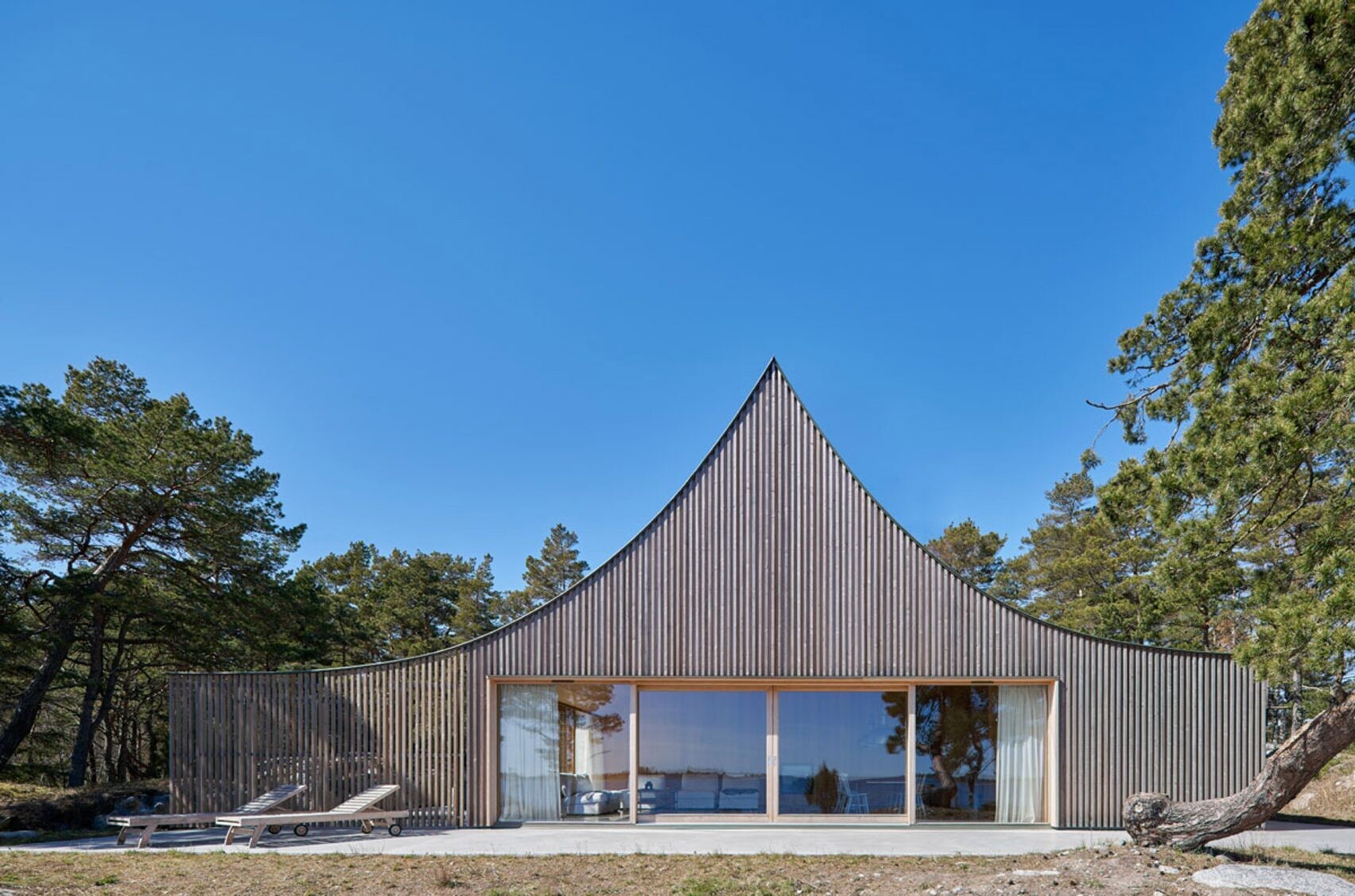 A sculptural cedar house by Tham & Videgård Arkitekter rises like a tent from the rocks of Krokholmen island, combining modern design with the simplicity of Swedish summer living.