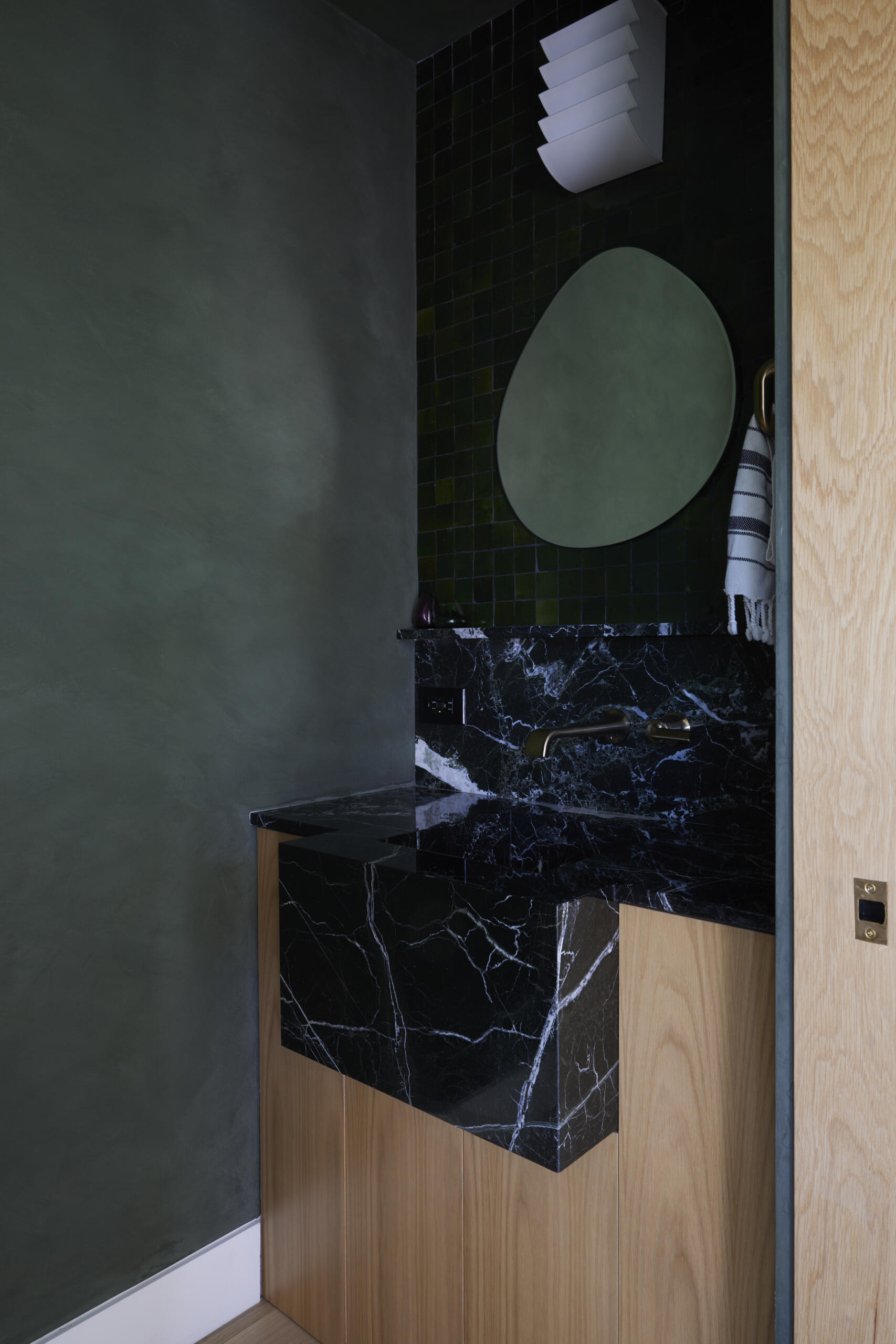 Moody and sculptural, the powder room features limewash walls and a cantilevered integrated stone sink that feels like a piece of art.