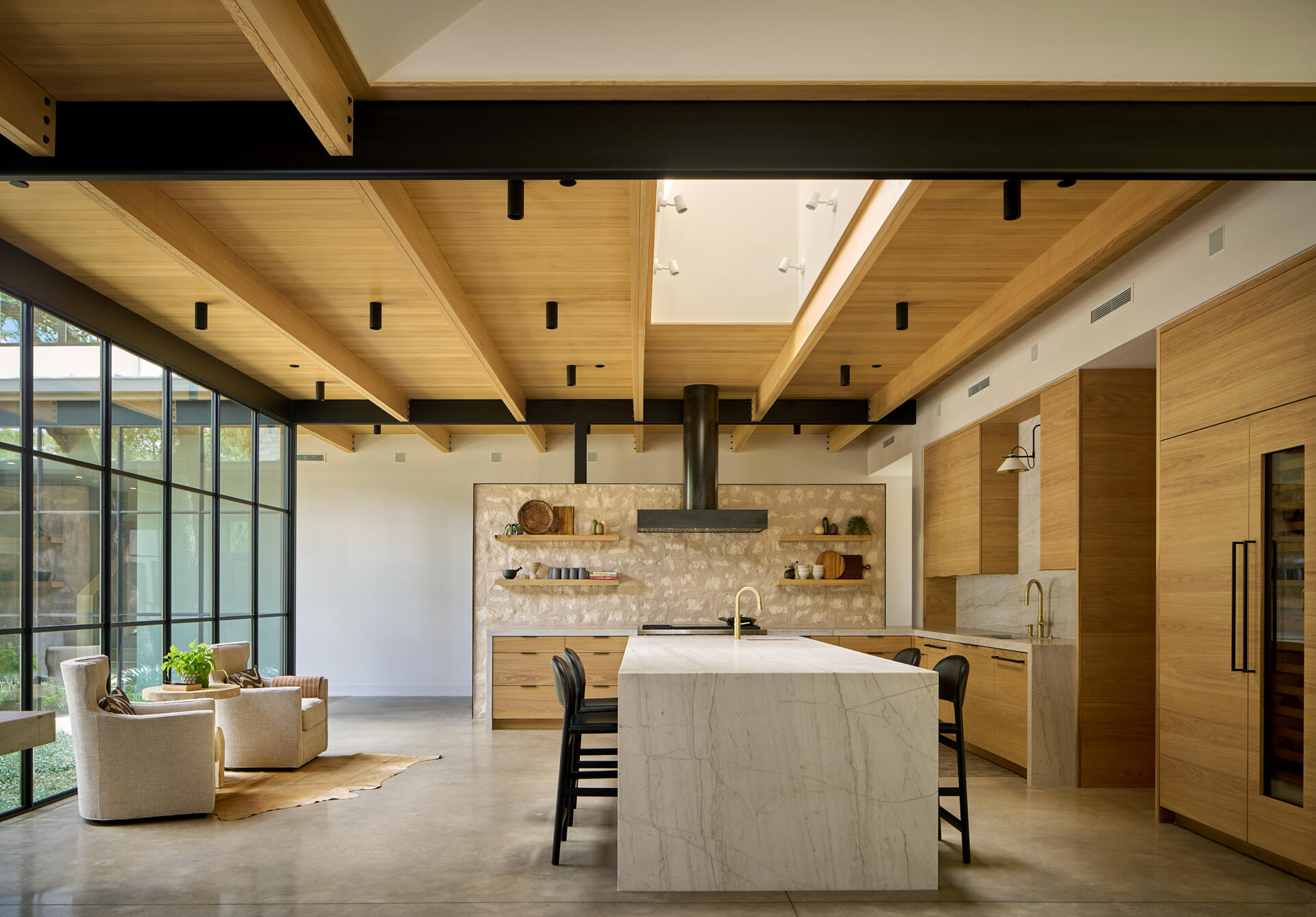The kitchen is a highlight, grounded by quarter sawn white oak cabinetry and a honed quartzite countertop. Above it, a Hemlock wood ceiling floats, punctured by a large skylight that floods the workspace with natural light. Brass fixtures bring subtle warmth, while stained concrete floors reflect brightness back into the space.