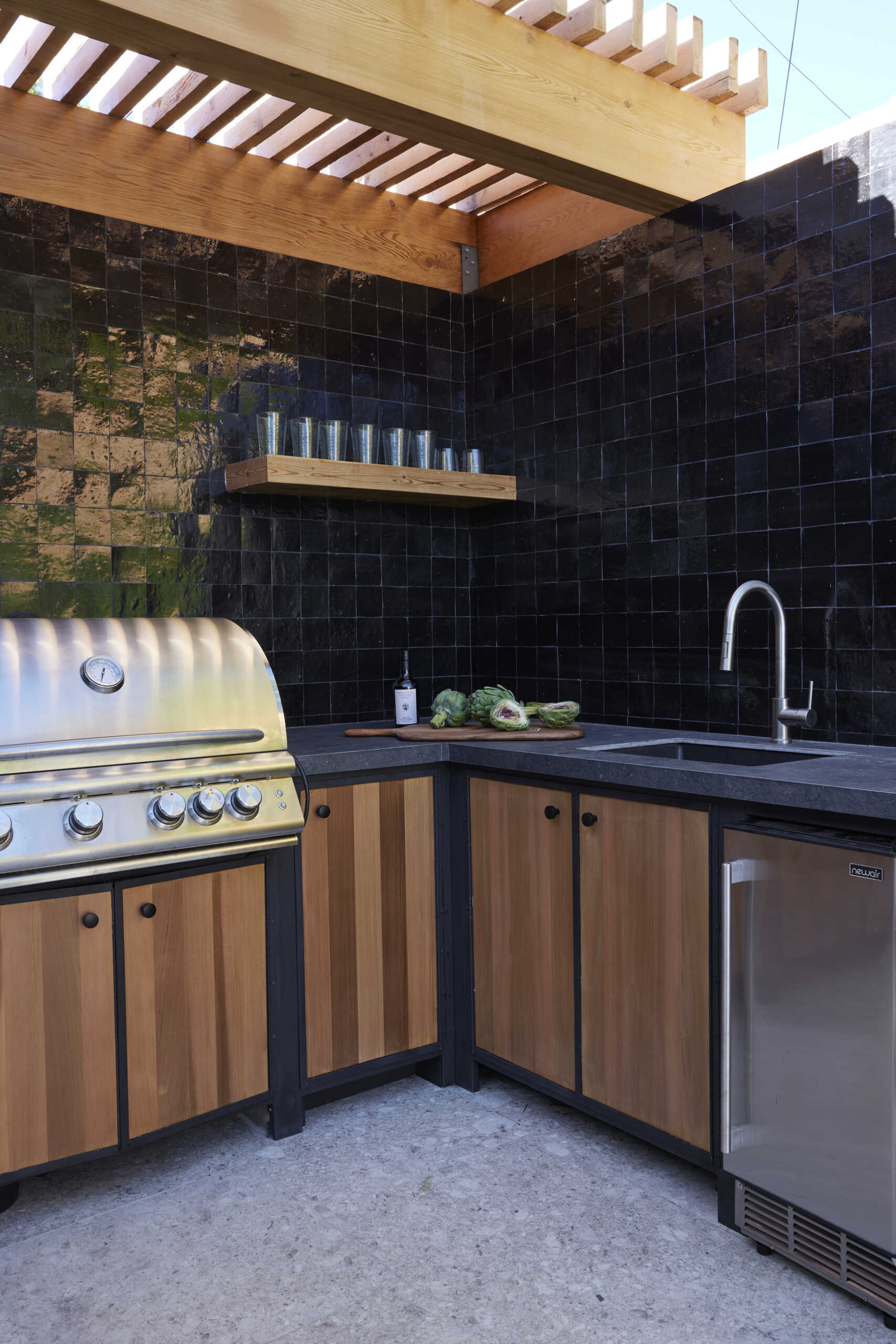 A full outdoor kitchen and tiled fire table extend living outdoors, creating a multifunctional space for cooking, entertaining, and gathering year-round.