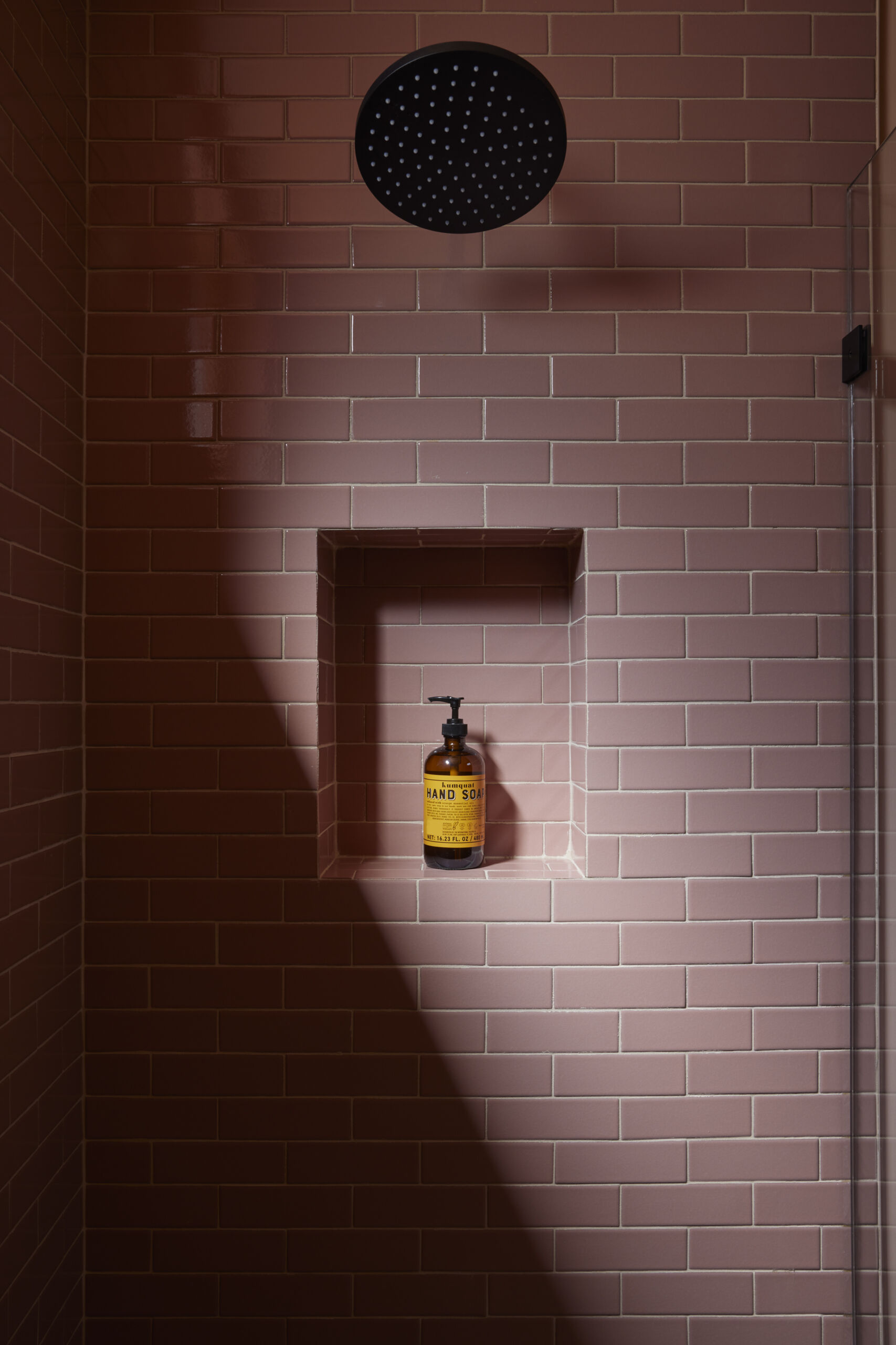 The guest bath carries thoughtful details and a soft pop of color with pink tiles and walls, while terrazzo flooring has a curbless transition and the shower niches combine function with precision.