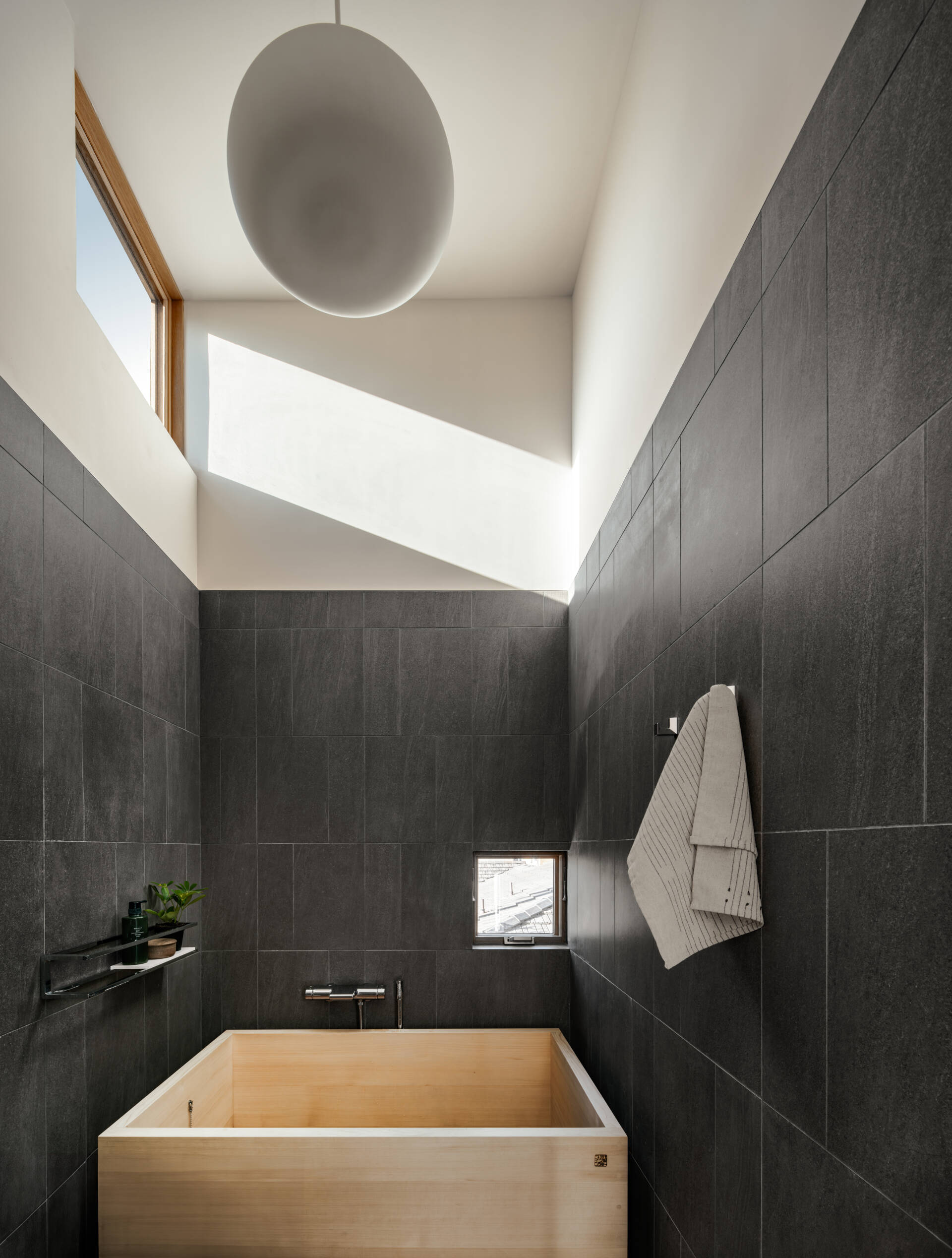 The upper floor houses the primary suite with a slate-clad wet room. A Japanese Ofuro soaking tub creates a tranquil retreat, blending minimalist design with sensory appeal. This suite emphasizes comfort and private indulgence within the compact footprint.