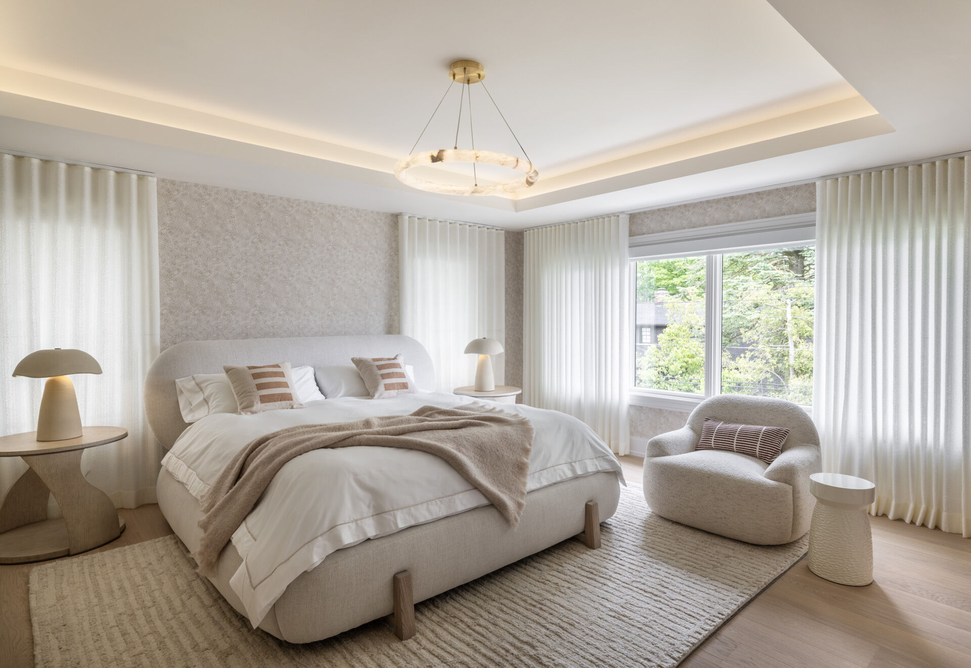 The primary bedroom keeps the palette hushed. Rounded edges, warm lamps, and upholstered textures dial up the comfort. It is generous without feeling grand. The real showpiece waits just beyond.