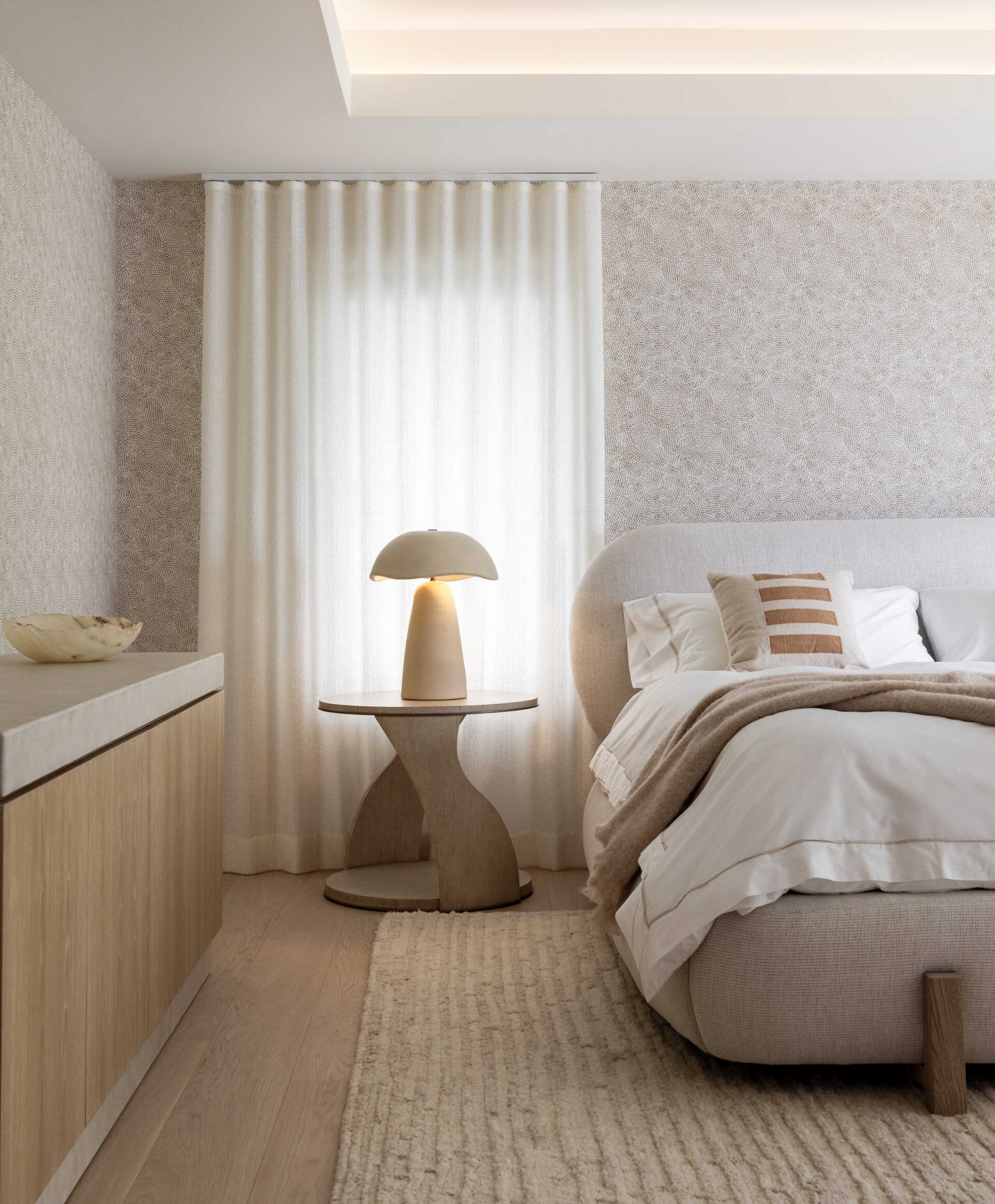 The primary bedroom keeps the palette hushed. Rounded edges, warm lamps, and upholstered textures dial up the comfort. It is generous without feeling grand. The real showpiece waits just beyond.
