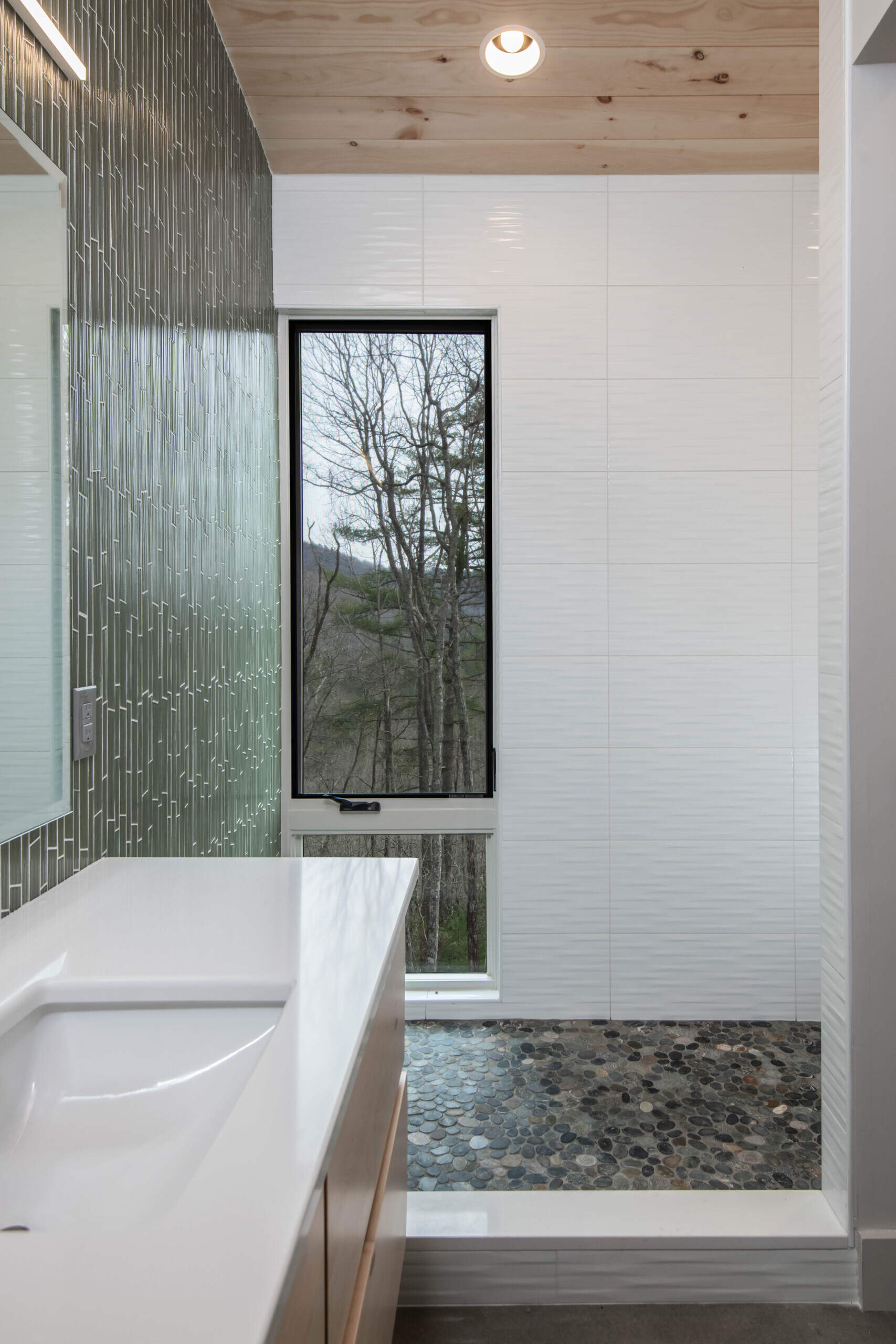 The bathroom features maple plywood details, textured white tiles and vertical green tiles. It offers a simple, functional space that aligns with the overall aesthetic while remaining comfortable for daily use.