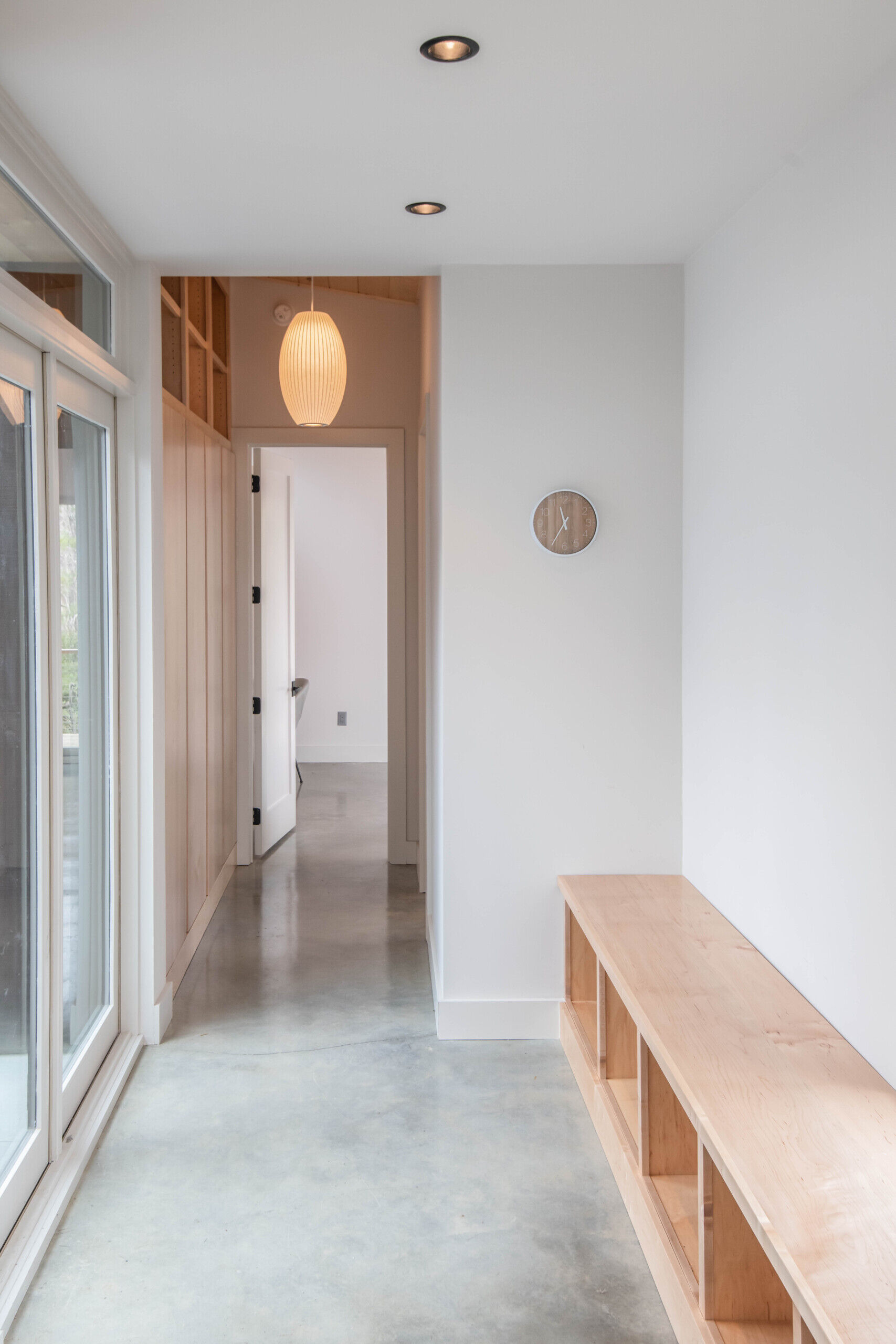 Inside, the entry continues the cabin’s minimalist aesthetic with polished concrete floors and subtle maple plywood built-ins for storage, keeping the space functional yet uncluttered.