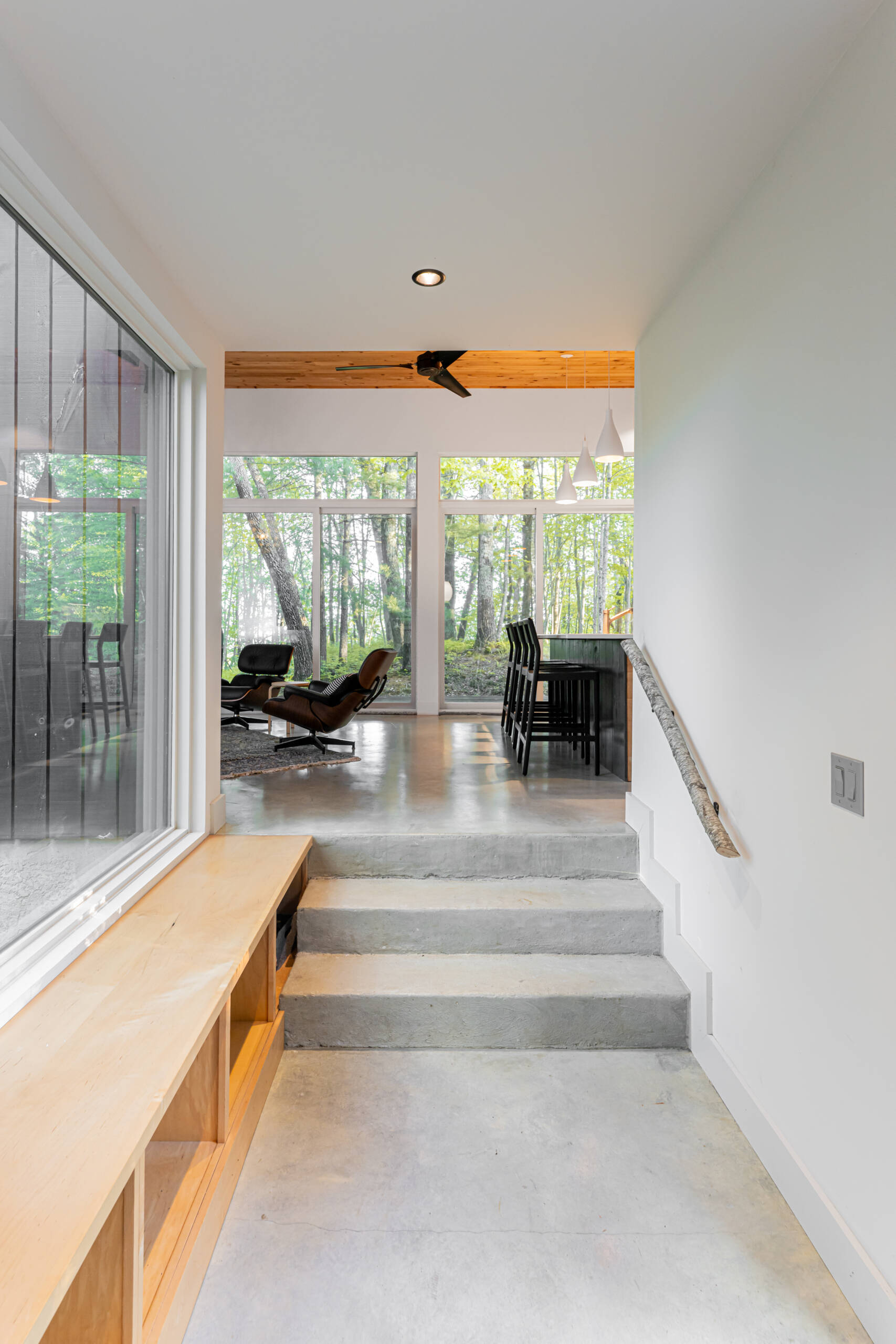 Inside, the entry continues the cabin’s minimalist aesthetic with polished concrete floors and subtle maple plywood built-ins for storage, keeping the space functional yet uncluttered.