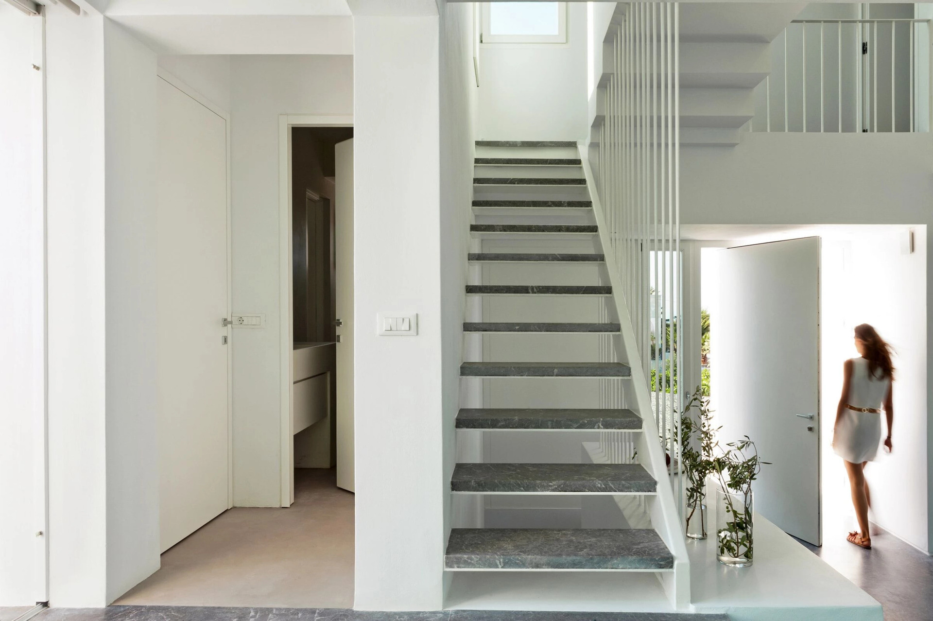 White cabinets blend into the walls, while Gortynis grey marble adds quiet sophistication to the stairs and hallway in this minimalist Greek home.