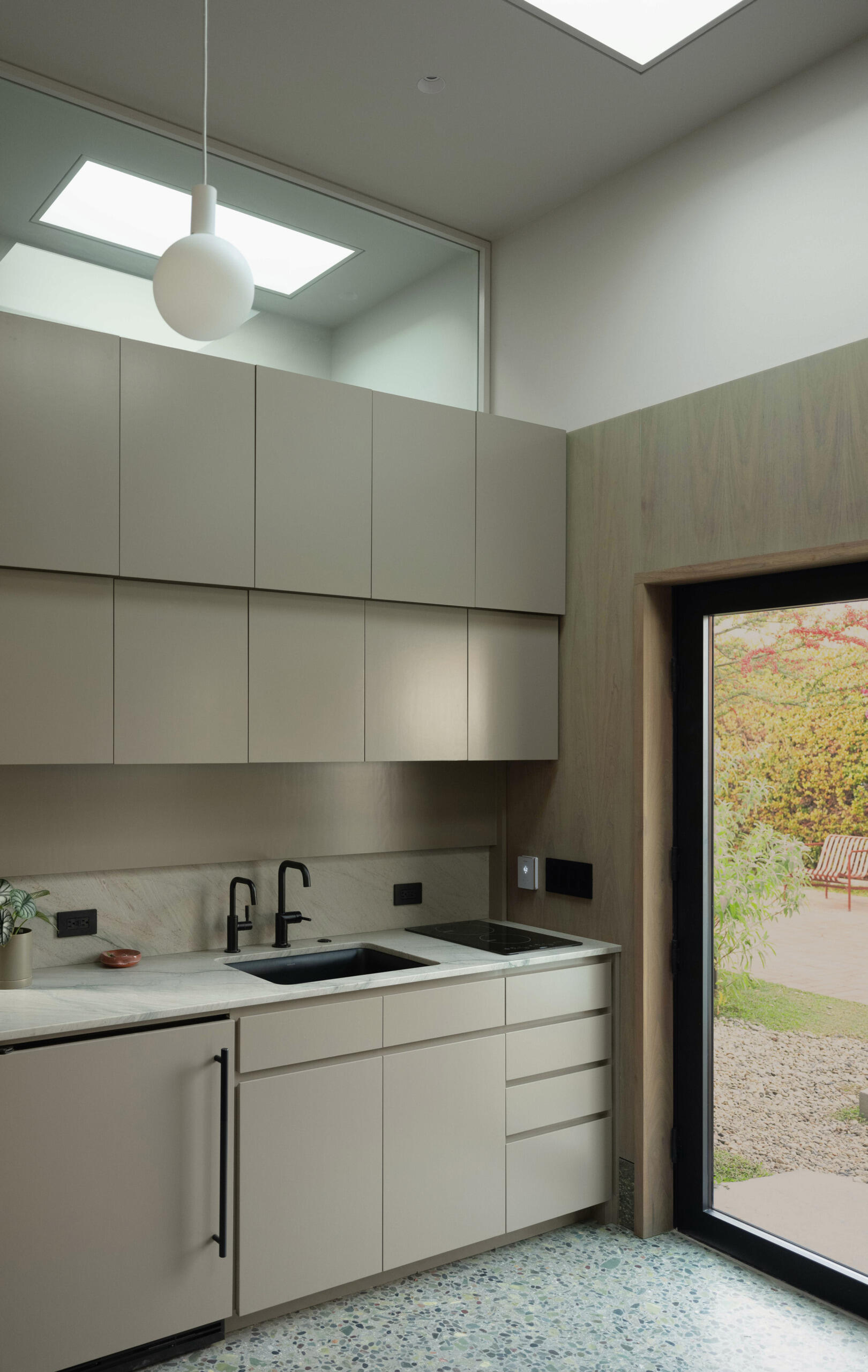 A green-tinted concrete floor and walnut cabinetry create a grounded, tactile kitchen where material textures and color interplay feel effortless and serene.