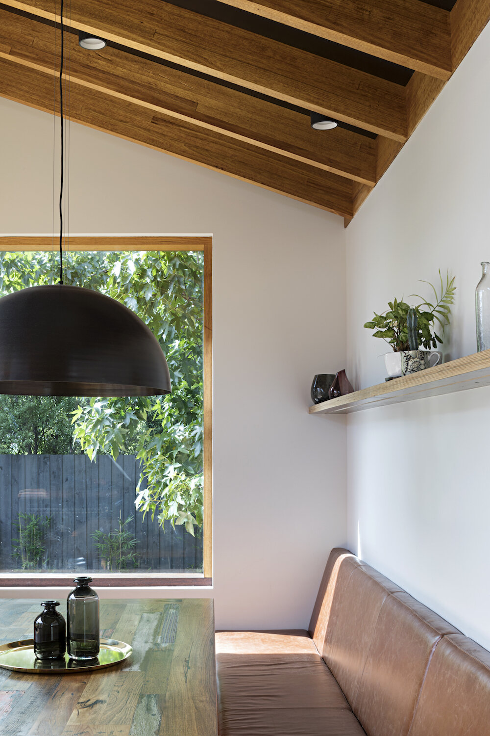 Restaurant style banquette seating wraps the corner of the extension and sits beneath a large window that frames views of the trees.