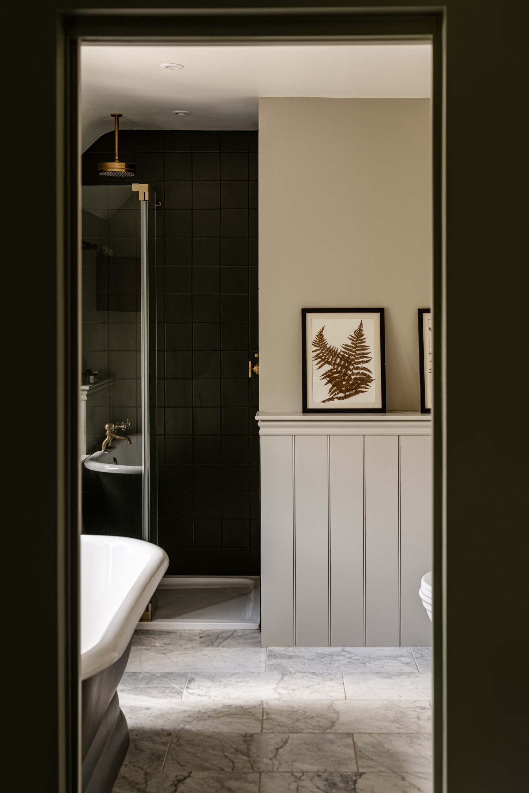 A calm bedroom painted in rich olive tones opens to a marble floored bathroom with a classic tub and dark tiled shower, while a warm walk-in wardrobe glows softly to the side. The layout feels intentional and serene, with each space connected by subtle light and thoughtful detailing.