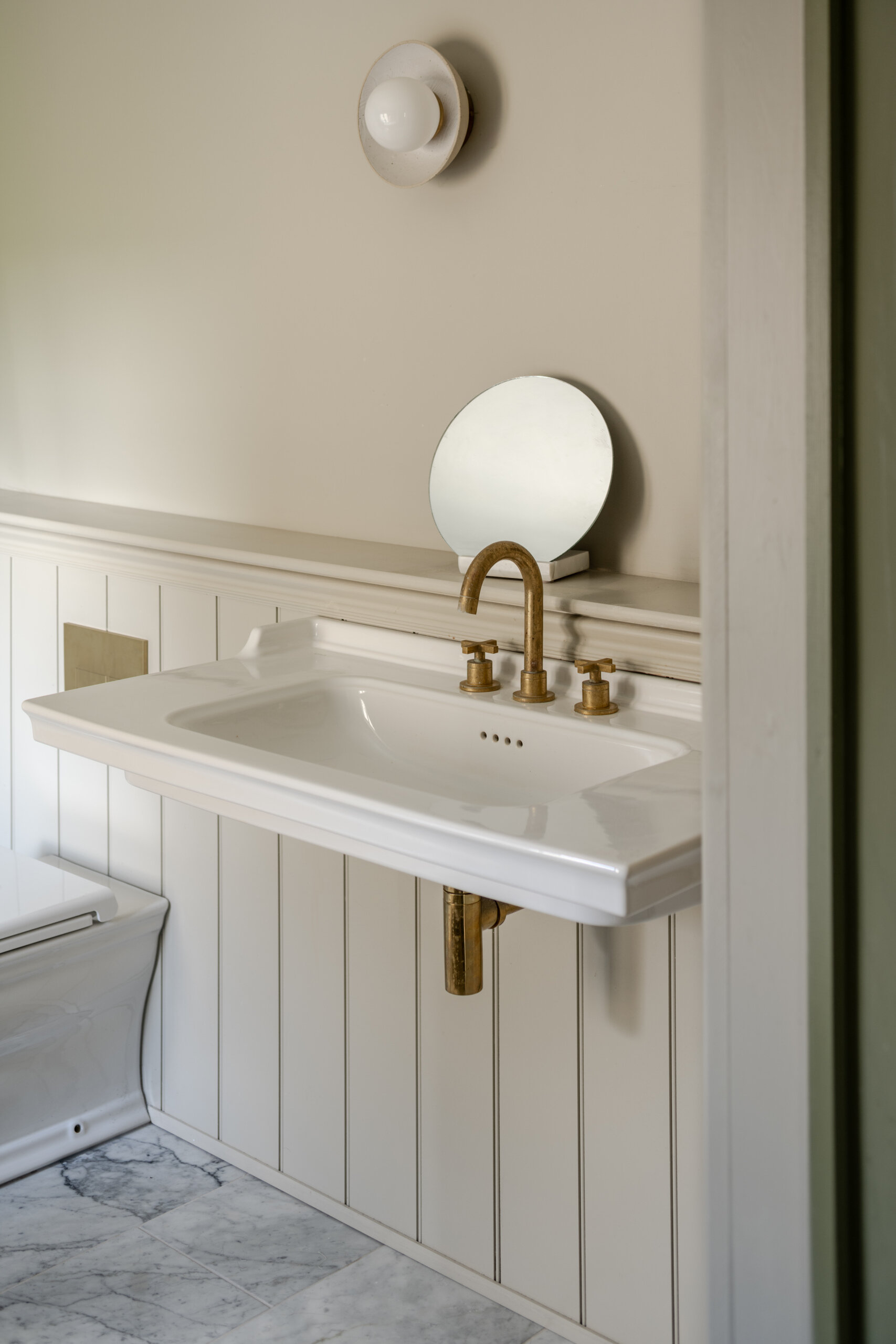 A calm bedroom painted in rich olive tones opens to a marble floored bathroom with a classic tub and dark tiled shower, while a warm walk-in wardrobe glows softly to the side. The layout feels intentional and serene, with each space connected by subtle light and thoughtful detailing.
