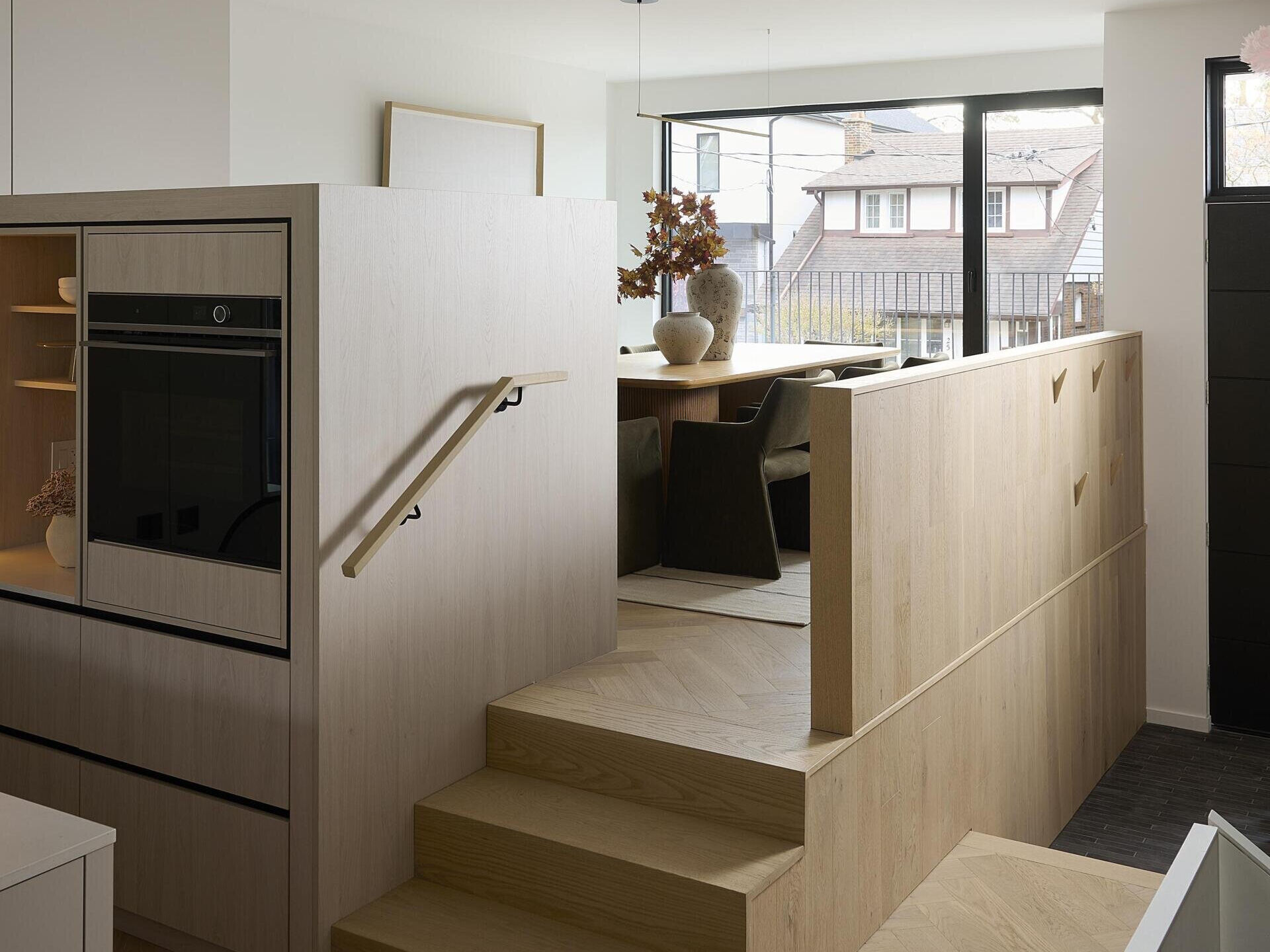 The dining area, accessed via a few steps, feels connected yet distinct, held by the warm tone of the oak cabinetry and the calm presence of the surrounding palette.