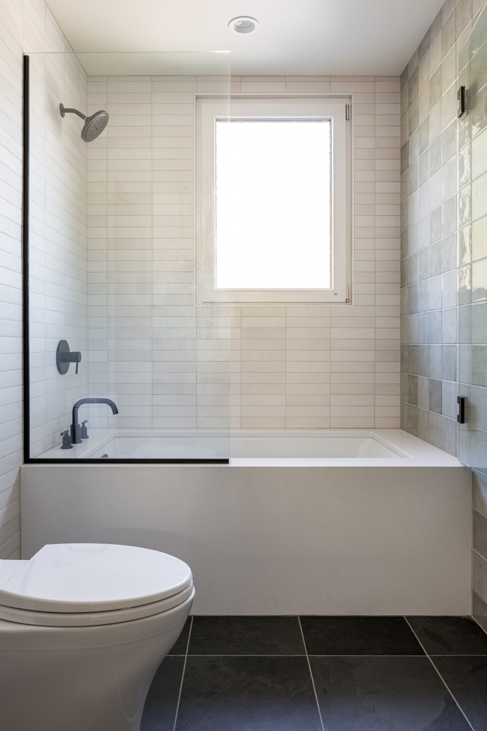 El baño en suite se mantiene limpio y tranquilo, diseñado para la relajación, con paredes cuadradas de azulejos grises y un tocador de madera flotante.