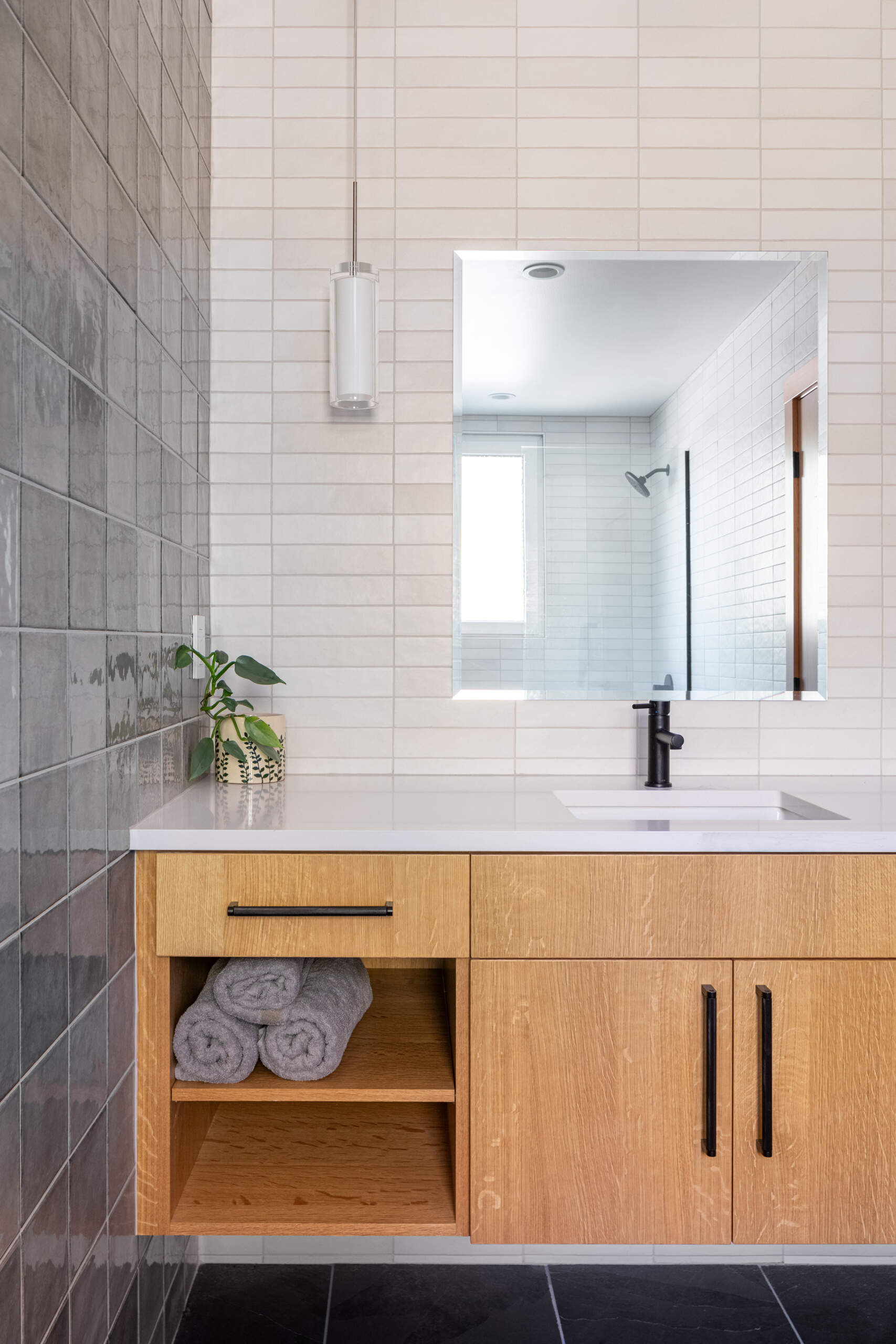 El baño en suite se mantiene limpio y tranquilo, diseñado para la relajación, con paredes cuadradas de azulejos grises y un tocador de madera flotante.