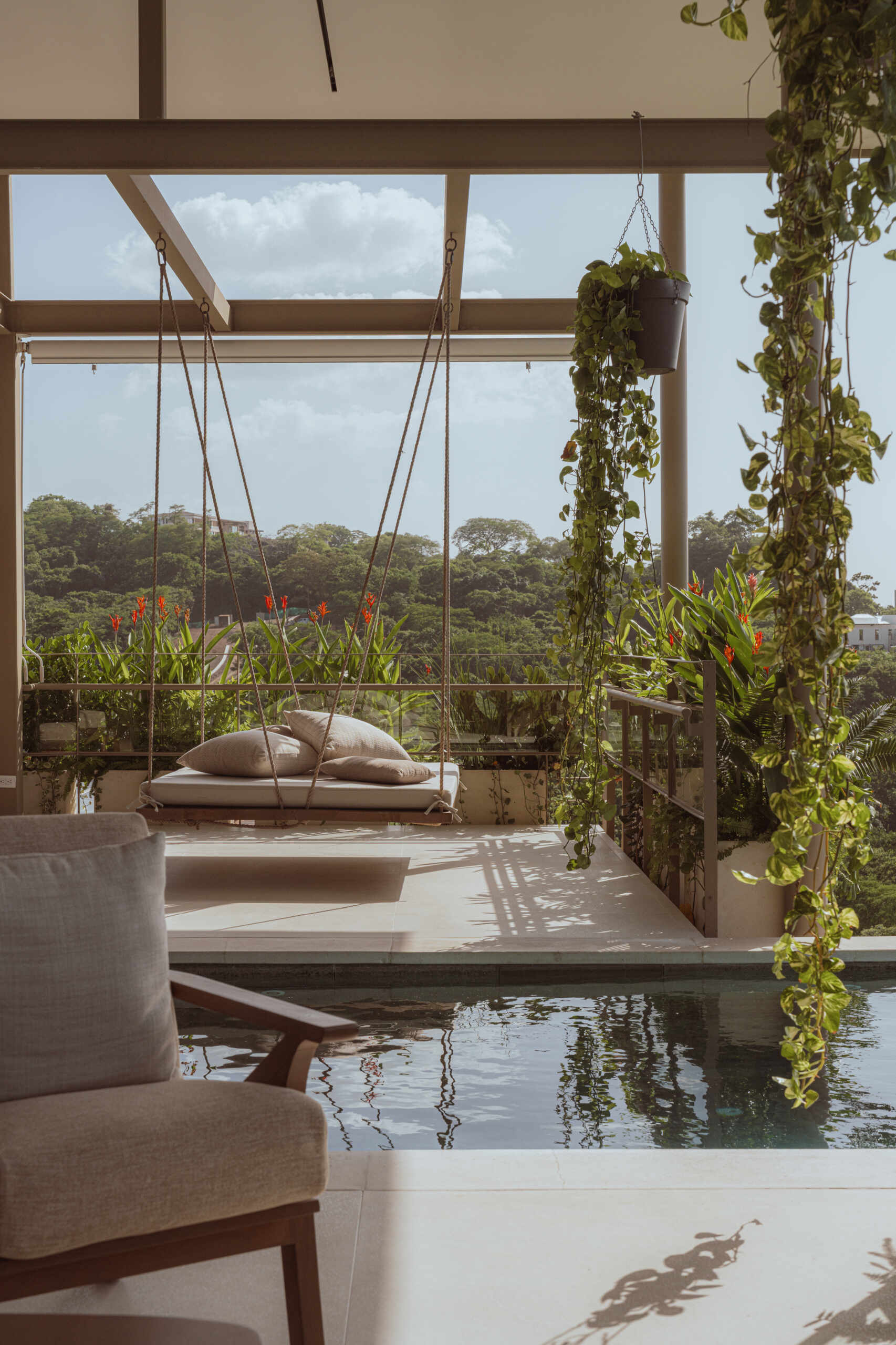 Terraces wrap around the social areas, creating outdoor lounges that feel naturally cooled by the surrounding vegetation. A suspended daybed adds a quieter, more restful zone, continuing the theme of soft transitions between spaces.