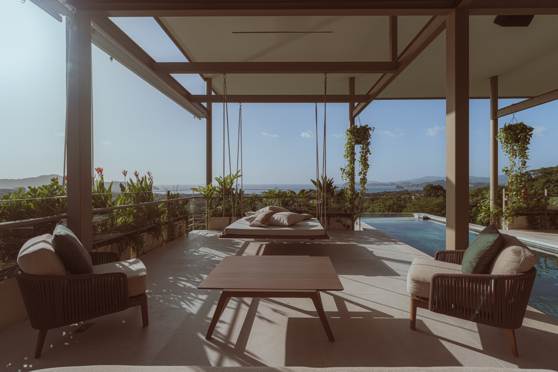 Terraces wrap around the social areas, creating outdoor lounges that feel naturally cooled by the surrounding vegetation. A suspended daybed adds a quieter, more restful zone, continuing the theme of soft transitions between spaces.