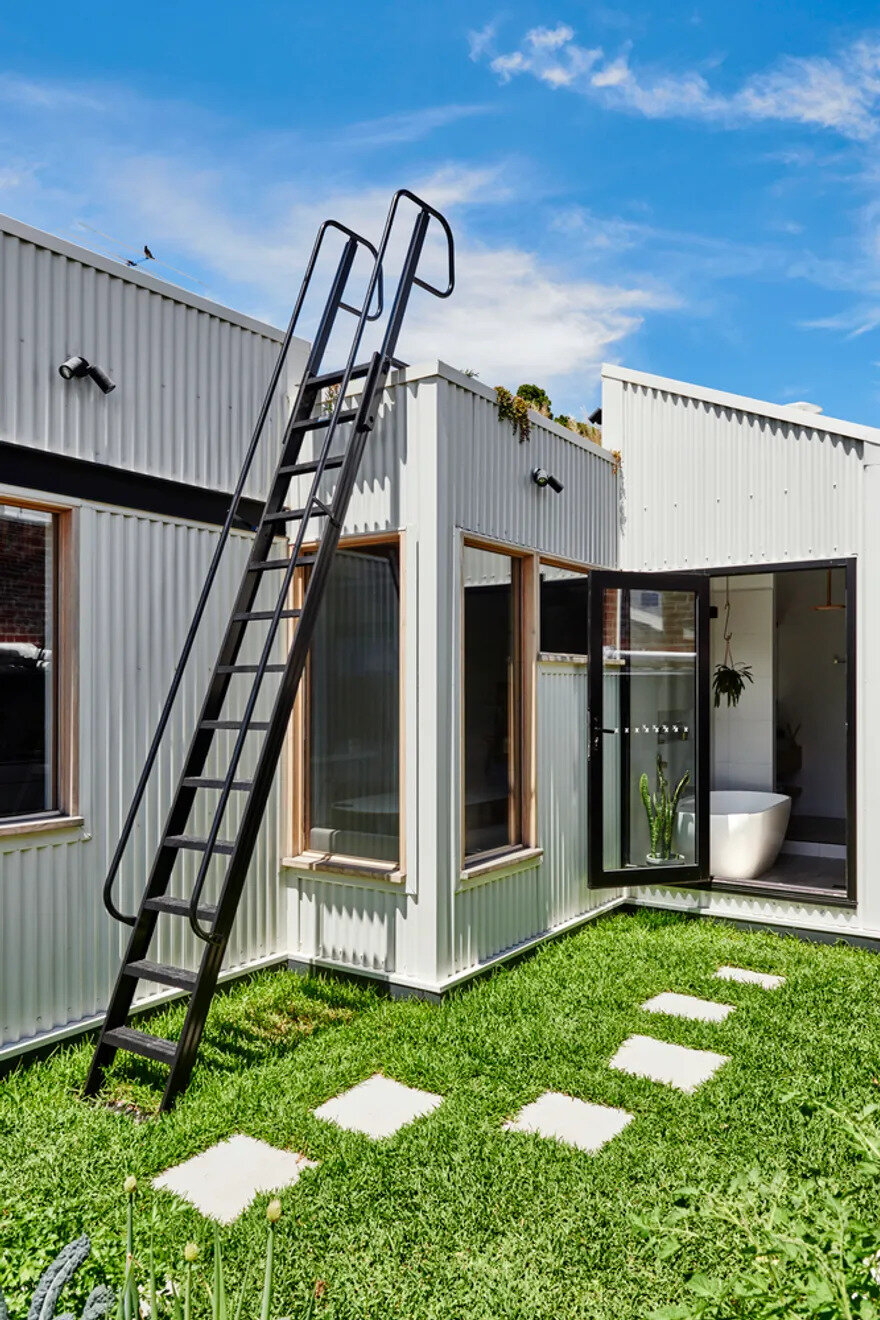 Stepping stones from the bathroom flow to a grassy outdoor spot that leads to a steel ladder and rooftop access.