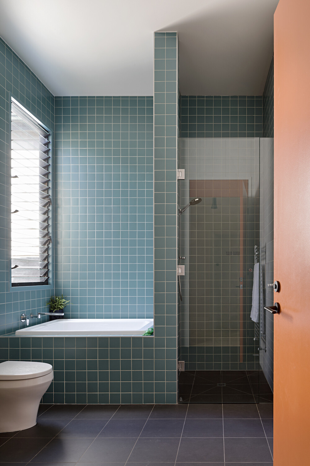 Square blue tiles with white grout surround a walk-in shower and half-size bath, giving this compact bathroom a bright and inviting look.